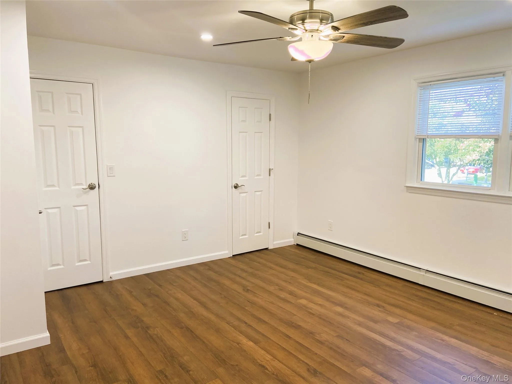 Unfurnished room featuring a baseboard radiator, ceiling fan, dark wood-type flooring, and baseboards Unfurnished room featuring a baseboard radiator, ceiling fan, dark wood-type flooring, and baseboards