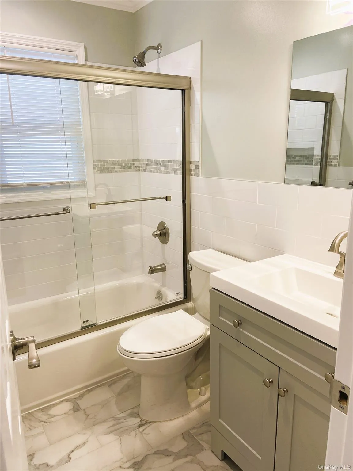 Full bath with vanity, toilet, enclosed tub / shower combo, and marble finish flooring Full bath with vanity, toilet, enclosed tub / shower combo, and marble finish flooring