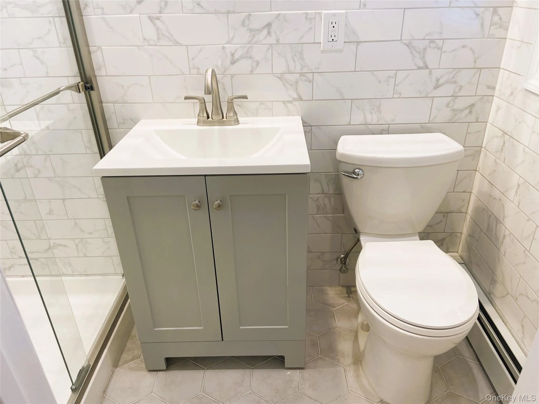 Full bath with toilet, vanity, a stall shower, tile walls, and a baseboard radiator Full bath with toilet, vanity, a stall shower, tile walls, and a baseboard radiator