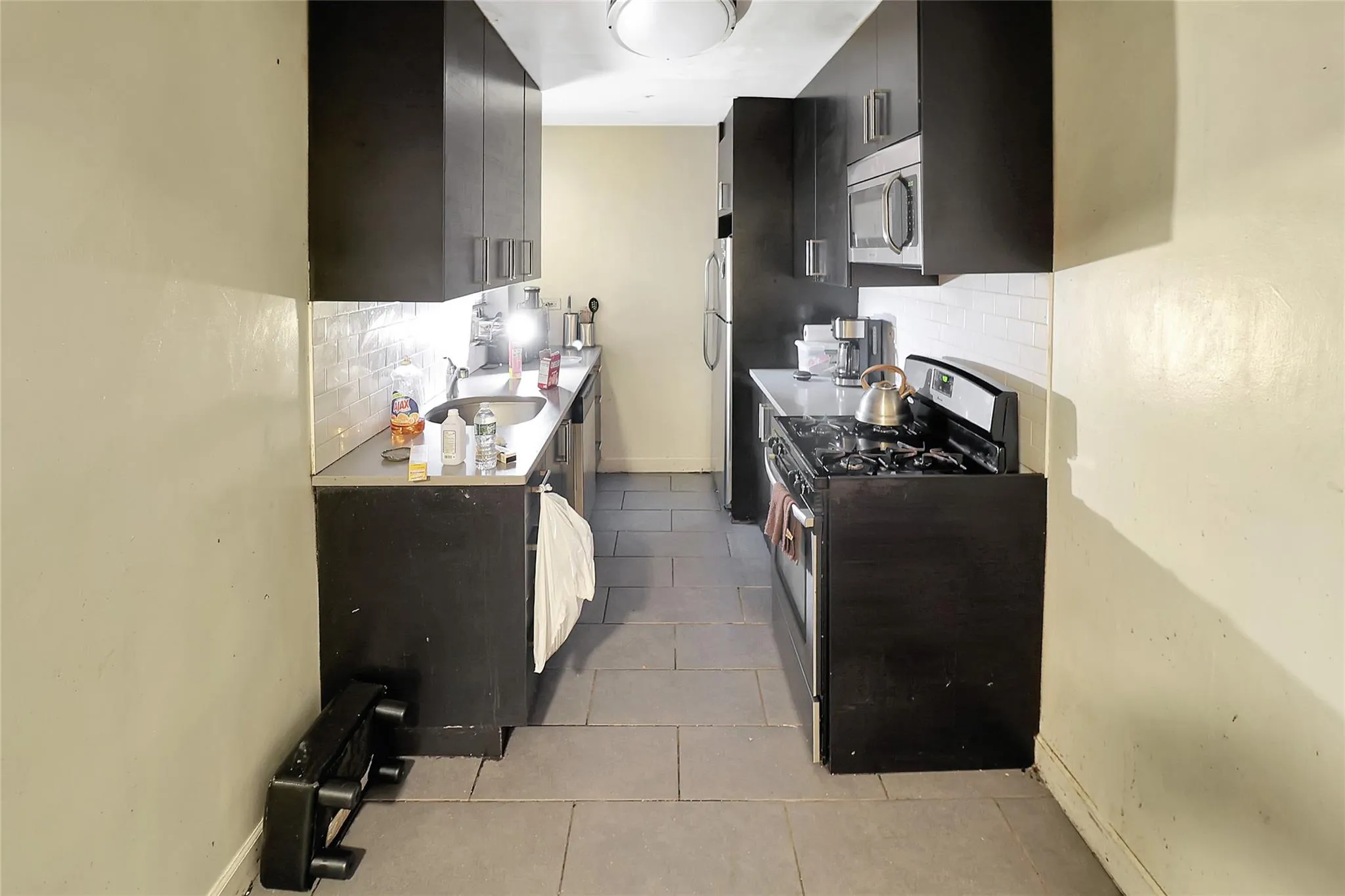 Kitchen featuring stainless steel appliances, dark cabinetry, backsplash, light tile patterned flooring, and light countertops Kitchen featuring stainless steel appliances, dark cabinetry, backsplash, light tile patterned flooring, and light countertops