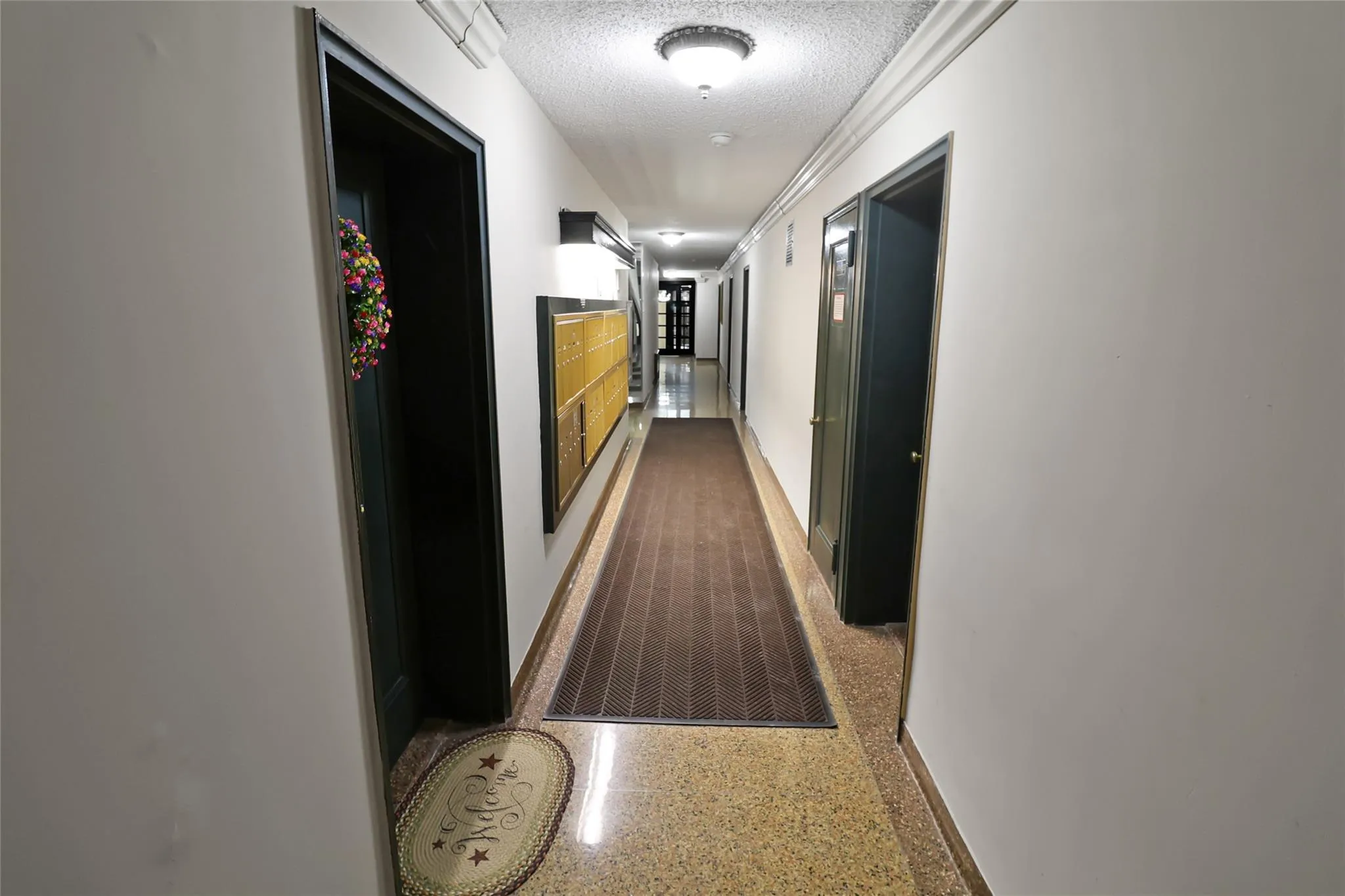 Hall with a textured ceiling, speckled floor, and baseboards Hall with a textured ceiling, speckled floor, and baseboards
