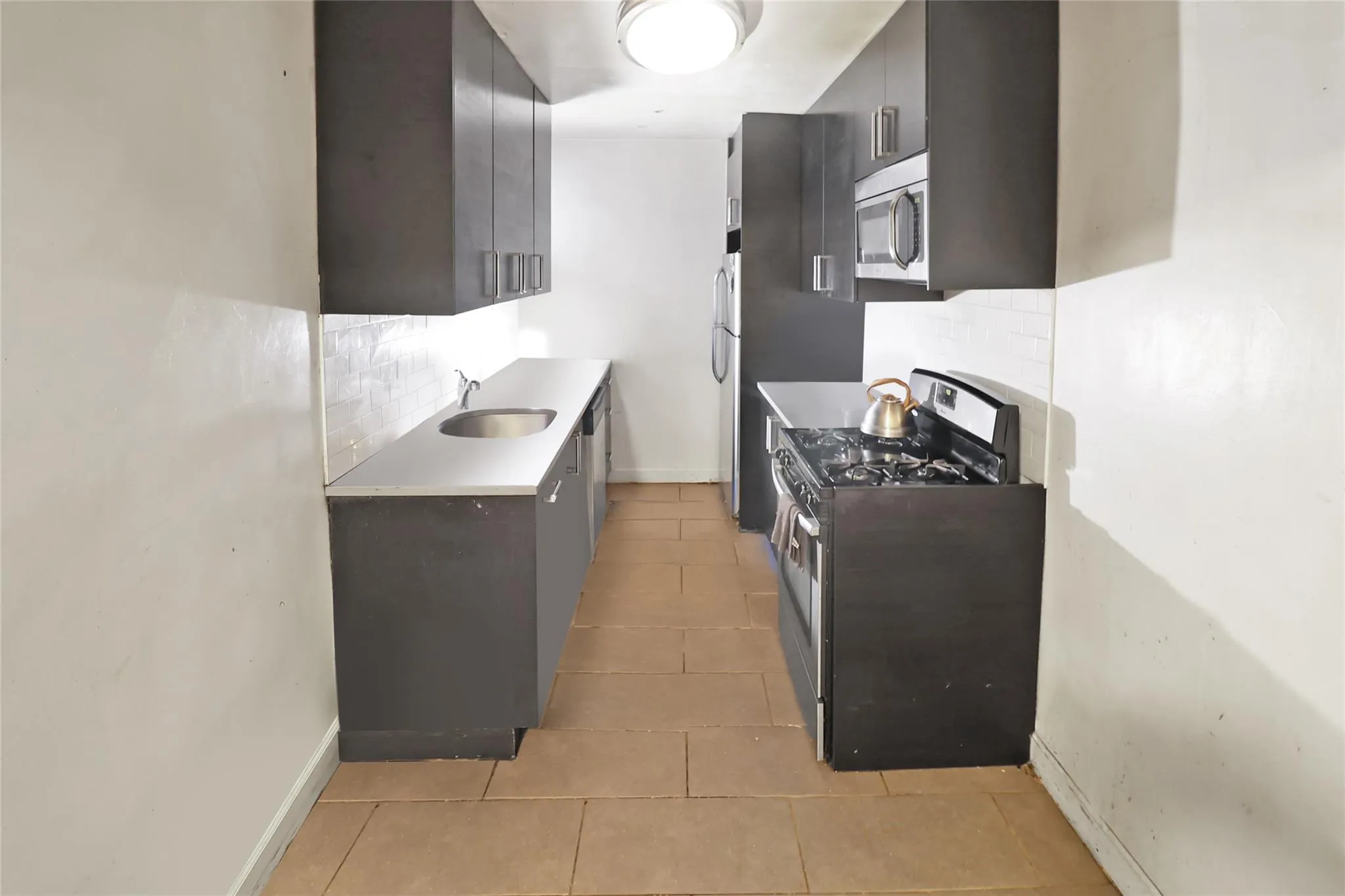 Kitchen featuring stainless steel appliances, backsplash, light tile patterned floors, a sink, and baseboards Kitchen featuring stainless steel appliances, backsplash, light tile patterned floors, a sink, and baseboards
