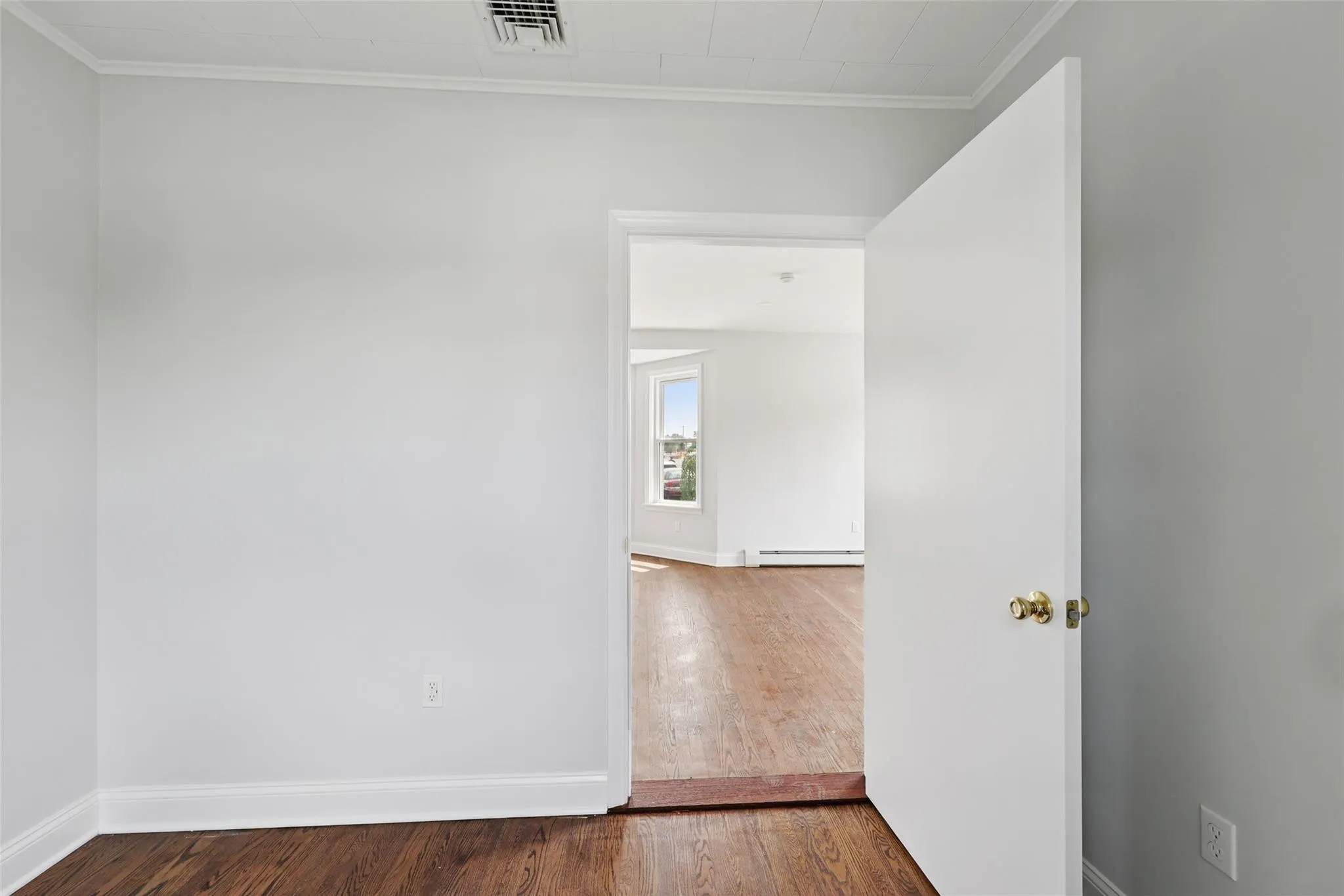 Unfurnished room featuring baseboard heating, crown molding, and wood finished floors Unfurnished room featuring baseboard heating, crown molding, and wood finished floors