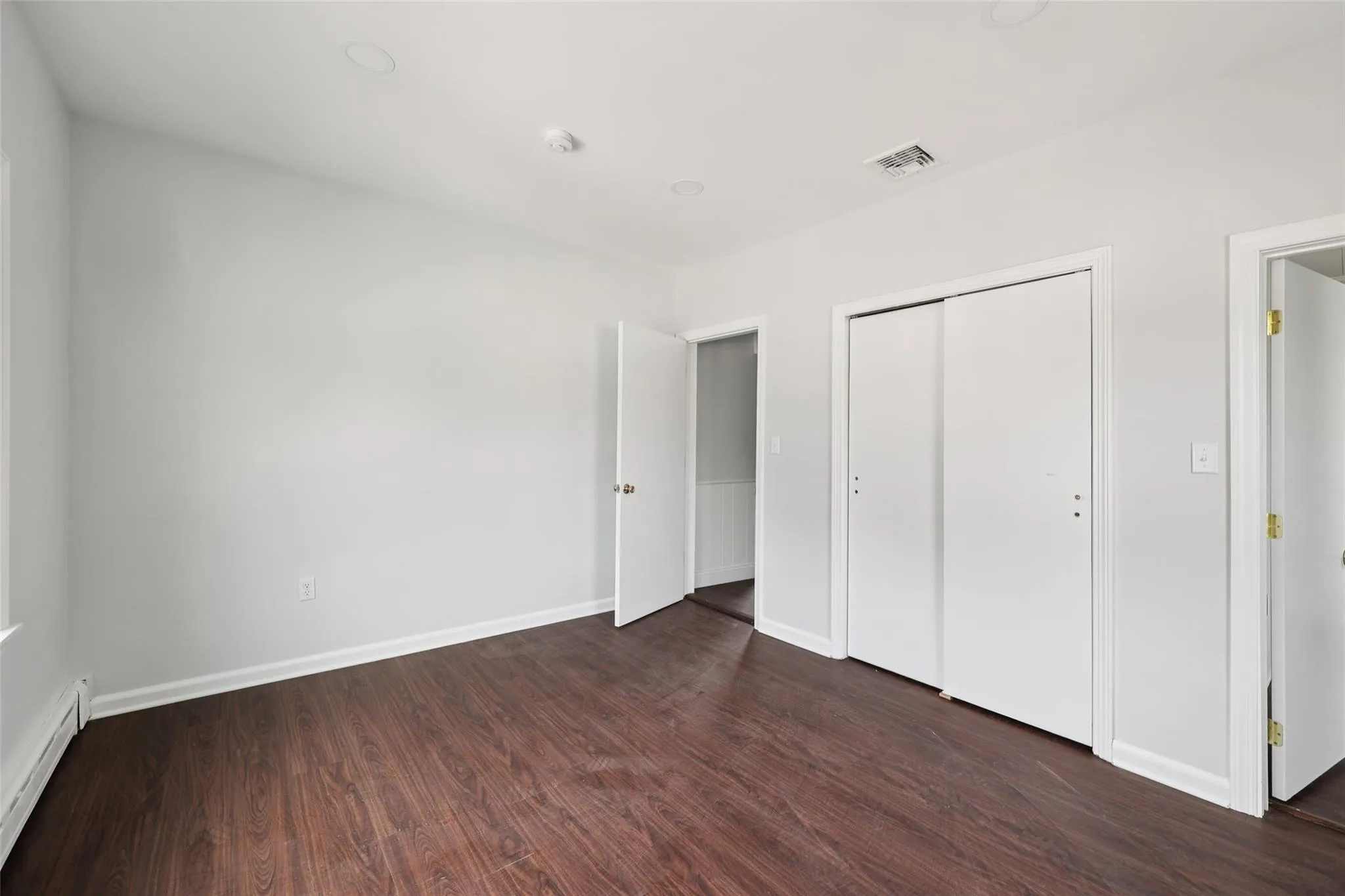 Unfurnished bedroom featuring a baseboard radiator, dark wood finished floors, and a closet Unfurnished bedroom featuring a baseboard radiator, dark wood finished floors, and a closet