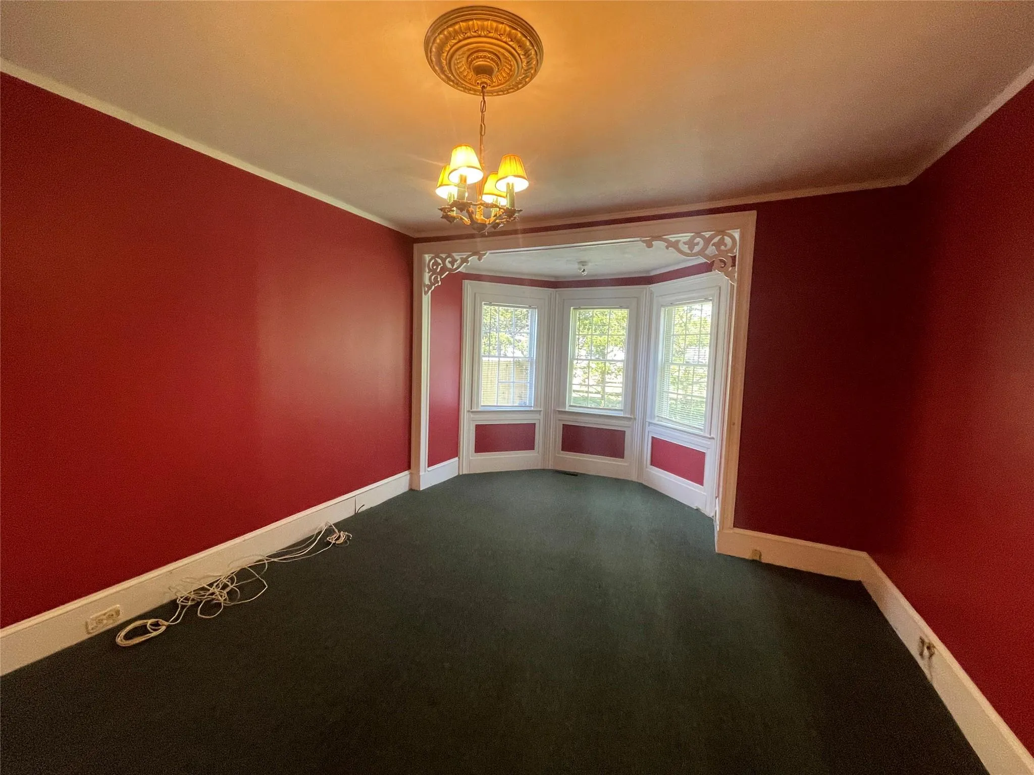 Empty room with a chandelier, dark colored carpet, and crown molding Empty room with a chandelier, dark colored carpet, and crown molding