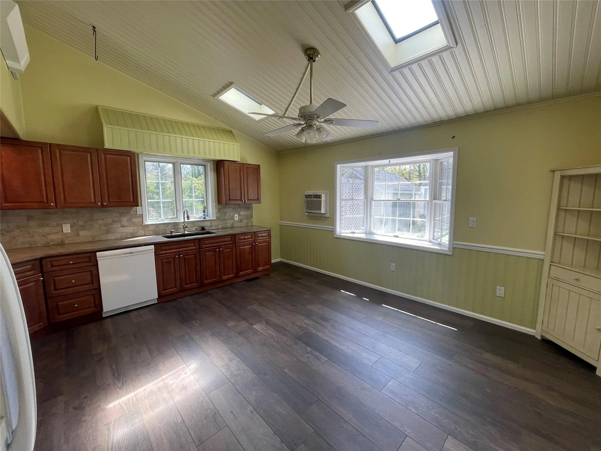 Kitchen featuring white dishwasher, a skylight, ceiling fan, a wainscoted wall, and dark wood-style floors Kitchen featuring white dishwasher, a skylight, ceiling fan, a wainscoted wall, and dark wood-style floors