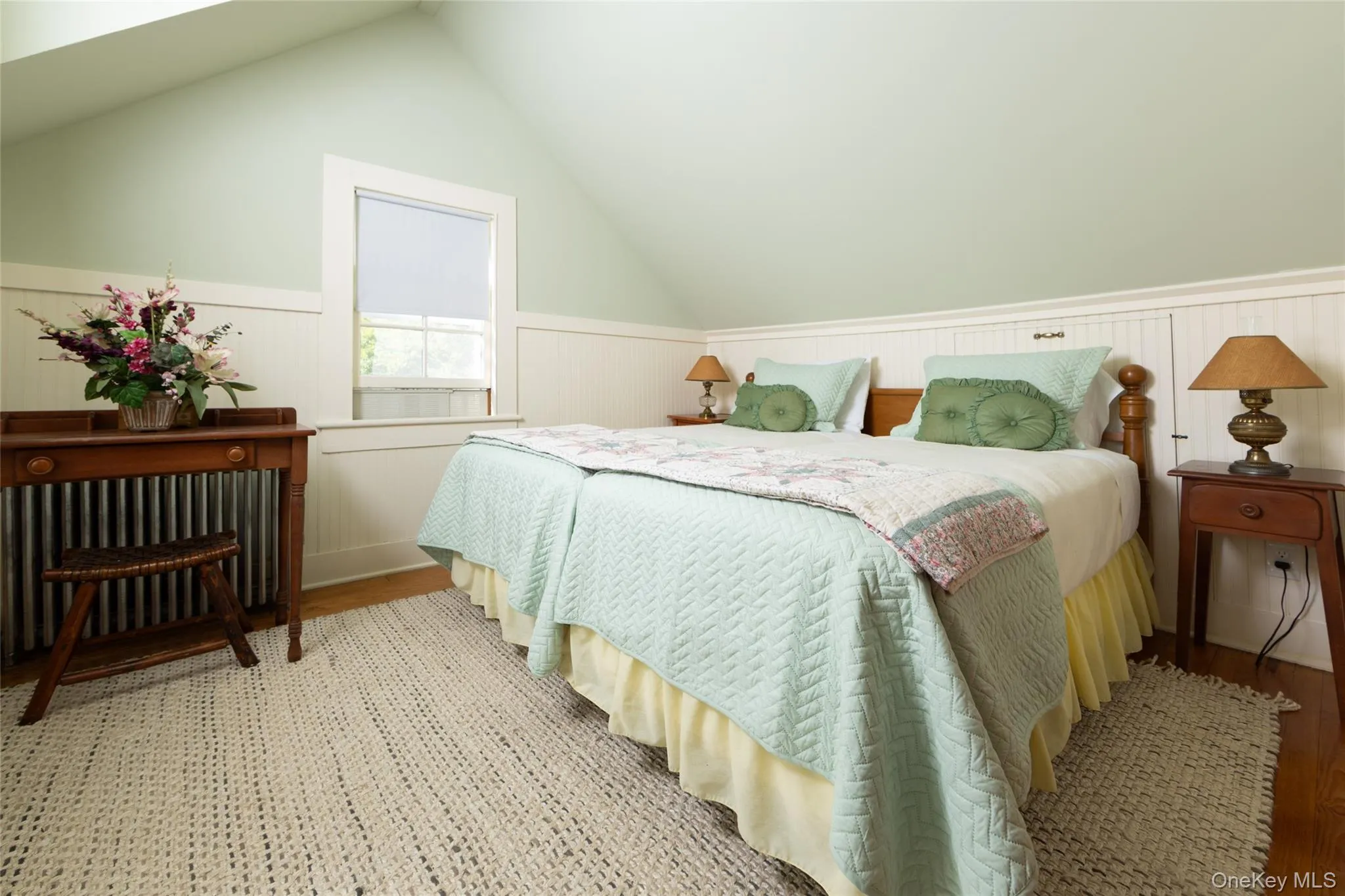 Bedroom with radiator, a wainscoted wall, light wood finished floors, and vaulted ceiling Bedroom with radiator, a wainscoted wall, light wood finished floors, and vaulted ceiling