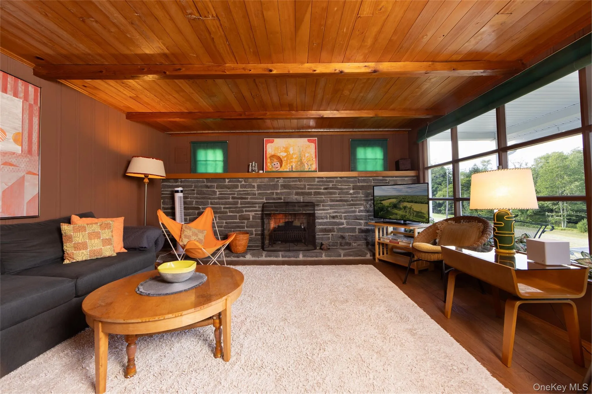 Living room featuring wooden ceiling with exposed beams, a stone fireplace, and wood finished floors Living room featuring wooden ceiling with exposed beams, a stone fireplace, and wood finished floors