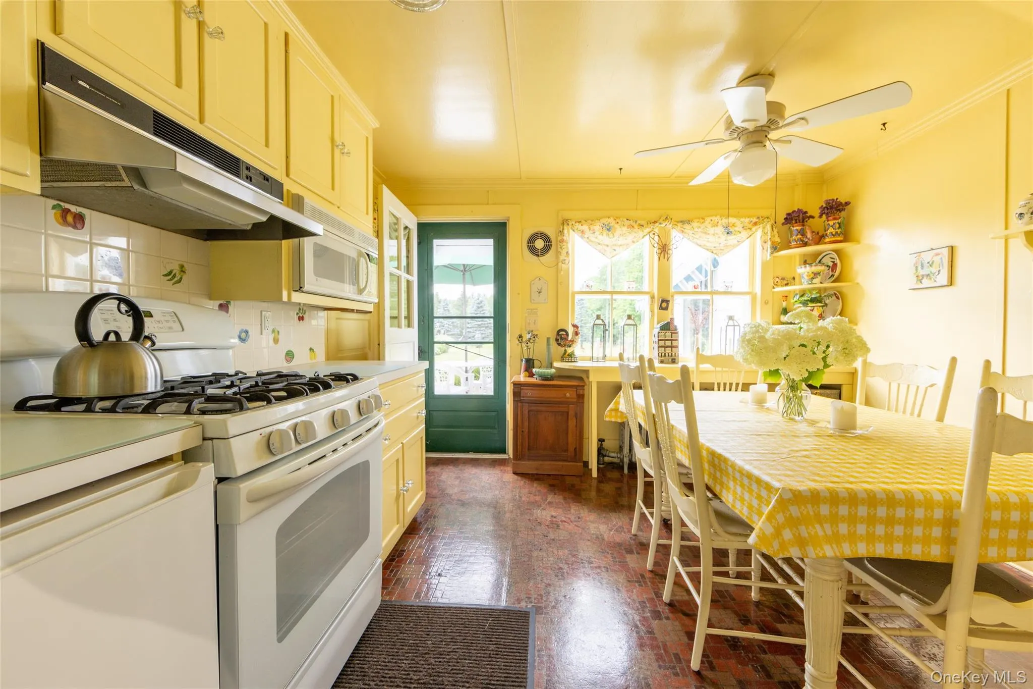 Kitchen featuring white appliances, under cabinet range hood, ornamental molding, a ceiling fan, and brick patterned floors Kitchen featuring white appliances, under cabinet range hood, ornamental molding, a ceiling fan, and brick patterned floors