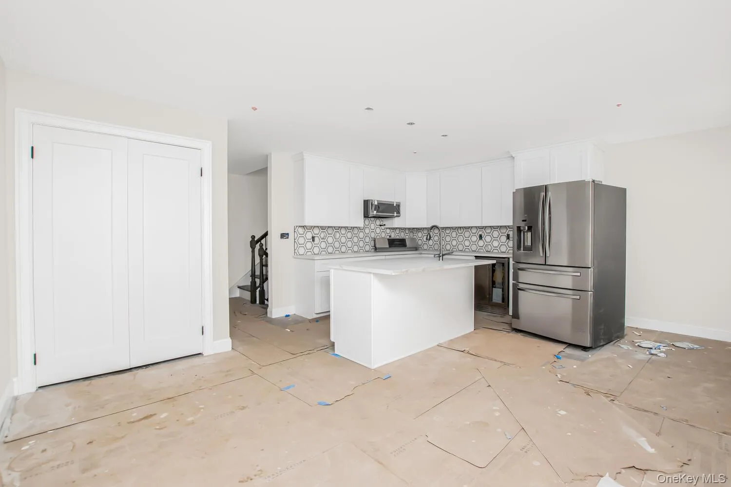 Kitchen featuring appliances with stainless steel finishes, backsplash, light countertops, a center island, and white cabinetry Kitchen featuring appliances with stainless steel finishes, backsplash, light countertops, a center island, and white cabinetry
