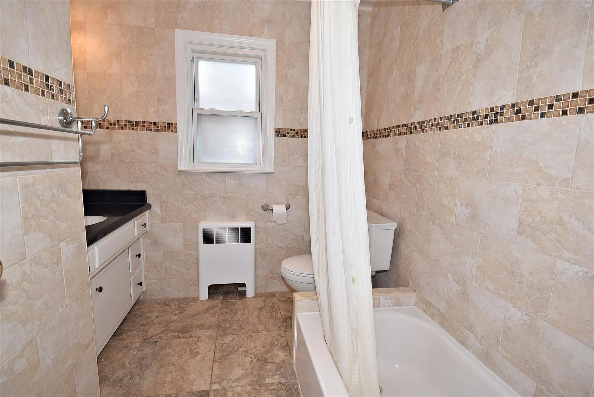 Bathroom with radiator, vanity, toilet, shower / bath combo, and tile walls Bathroom with radiator, vanity, toilet, shower / bath combo, and tile walls
