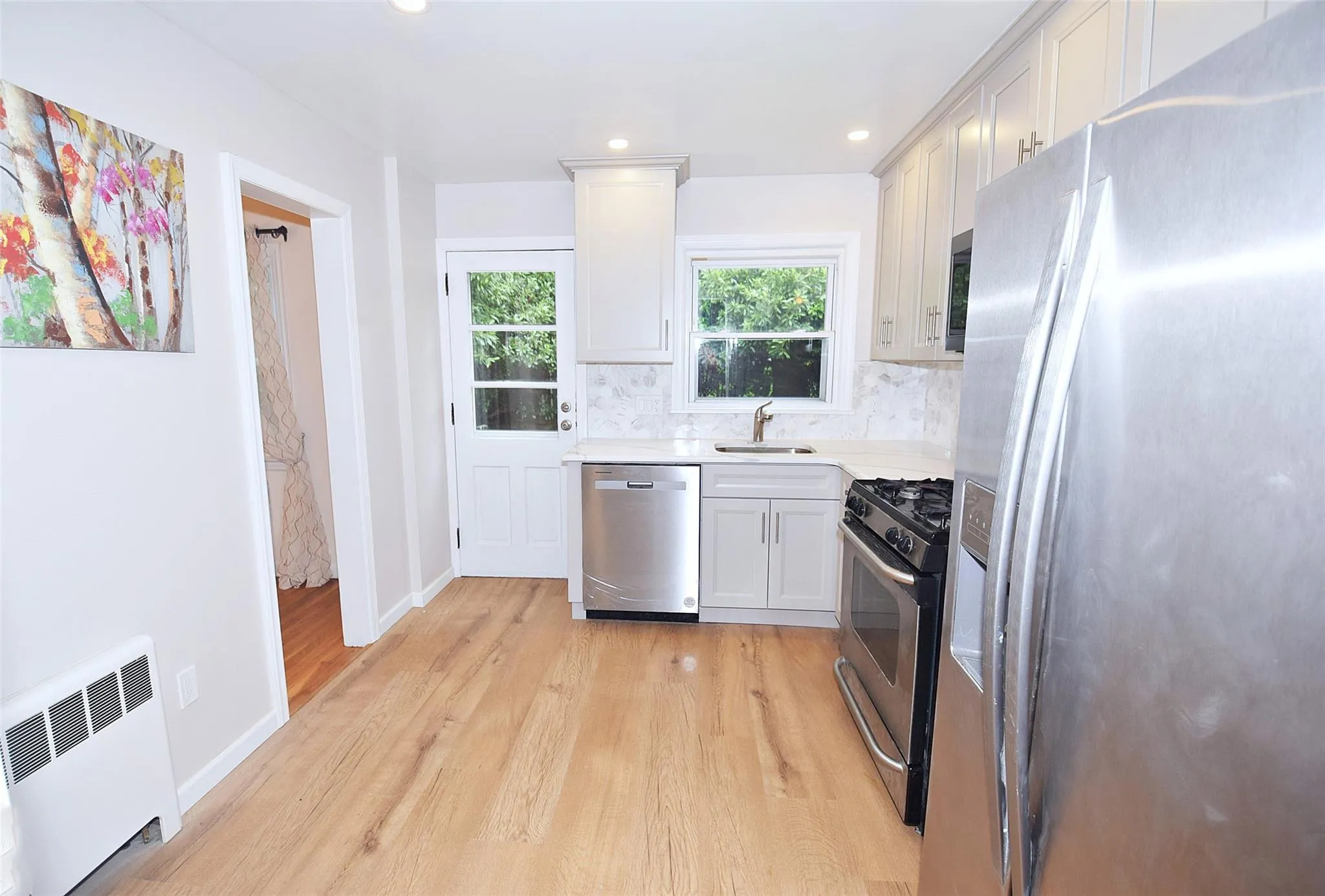 Kitchen with appliances with stainless steel finishes, radiator heating unit, light wood finished floors, light countertops, and decorative backsplash Kitchen with appliances with stainless steel finishes, radiator heating unit, light wood finished floors, light countertops, and decorative backsplash