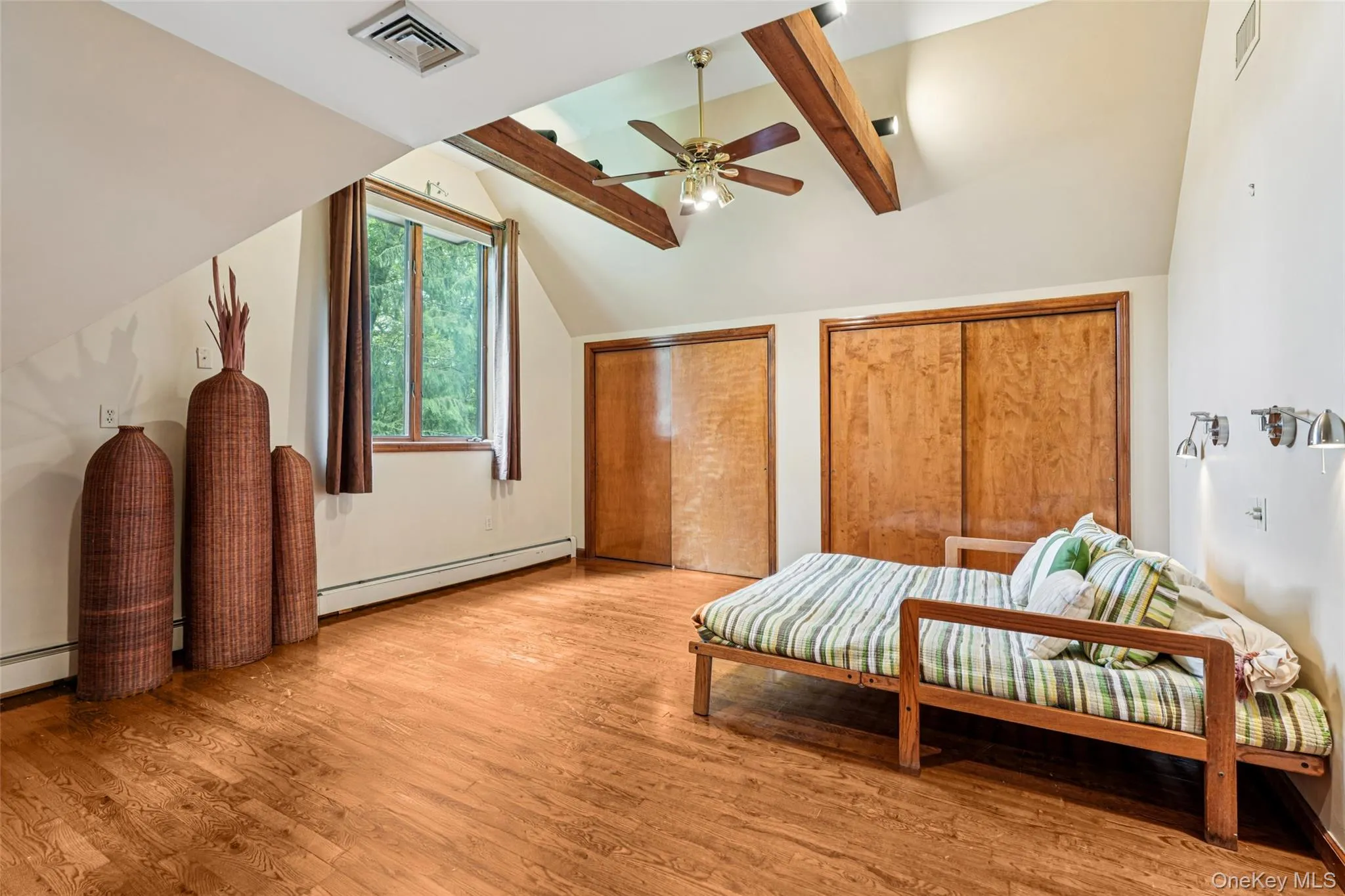 Bedroom with a baseboard radiator, light wood finished floors, two closets, and ceiling fan Bedroom with a baseboard radiator, light wood finished floors, two closets, and ceiling fan