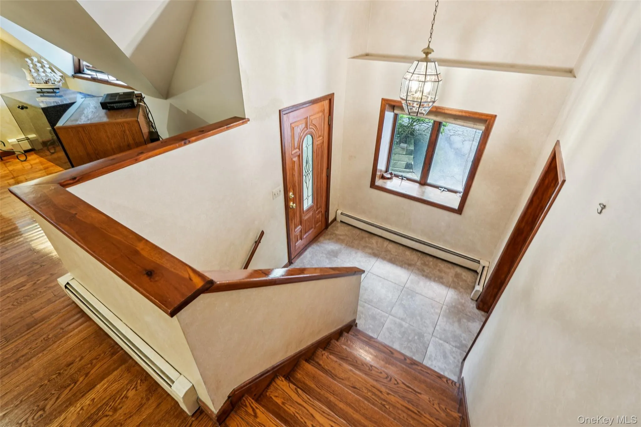 Staircase featuring baseboard heating, a baseboard heating unit, a chandelier, a towering ceiling, and wood finished floors Staircase featuring baseboard heating, a baseboard heating unit, a chandelier, a towering ceiling, and wood finished floors