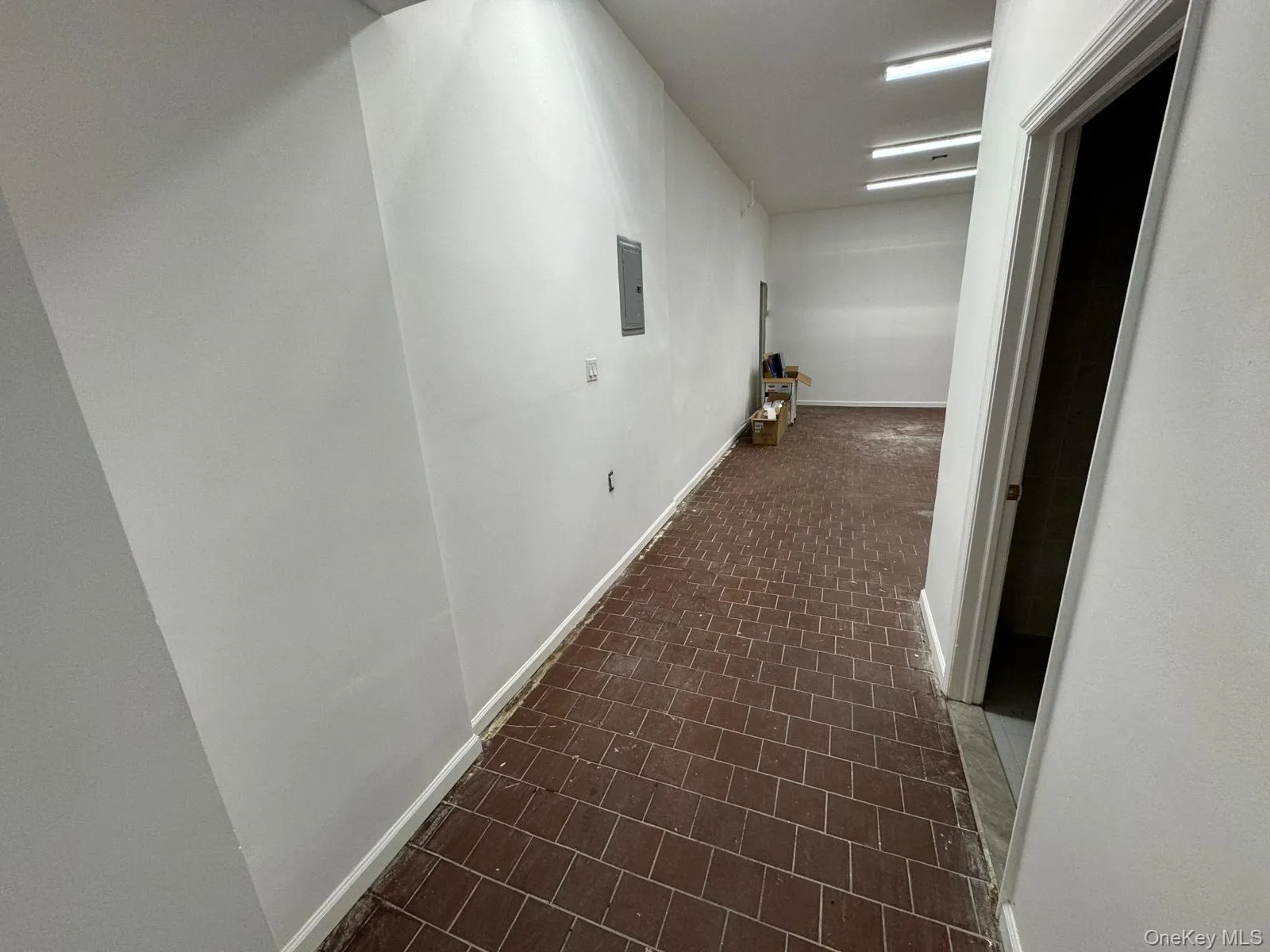 Corridor with brick patterned flooring, baseboards, and electric panel Corridor with brick patterned flooring, baseboards, and electric panel