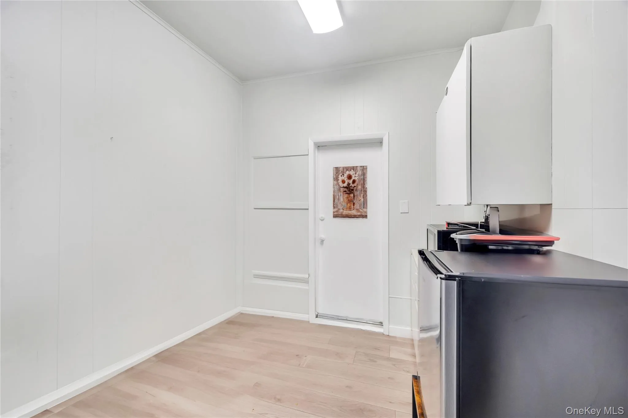 Kitchen with fridge, light wood-style flooring, dark countertops, crown molding, and white cabinets Kitchen with fridge, light wood-style flooring, dark countertops, crown molding, and white cabinets