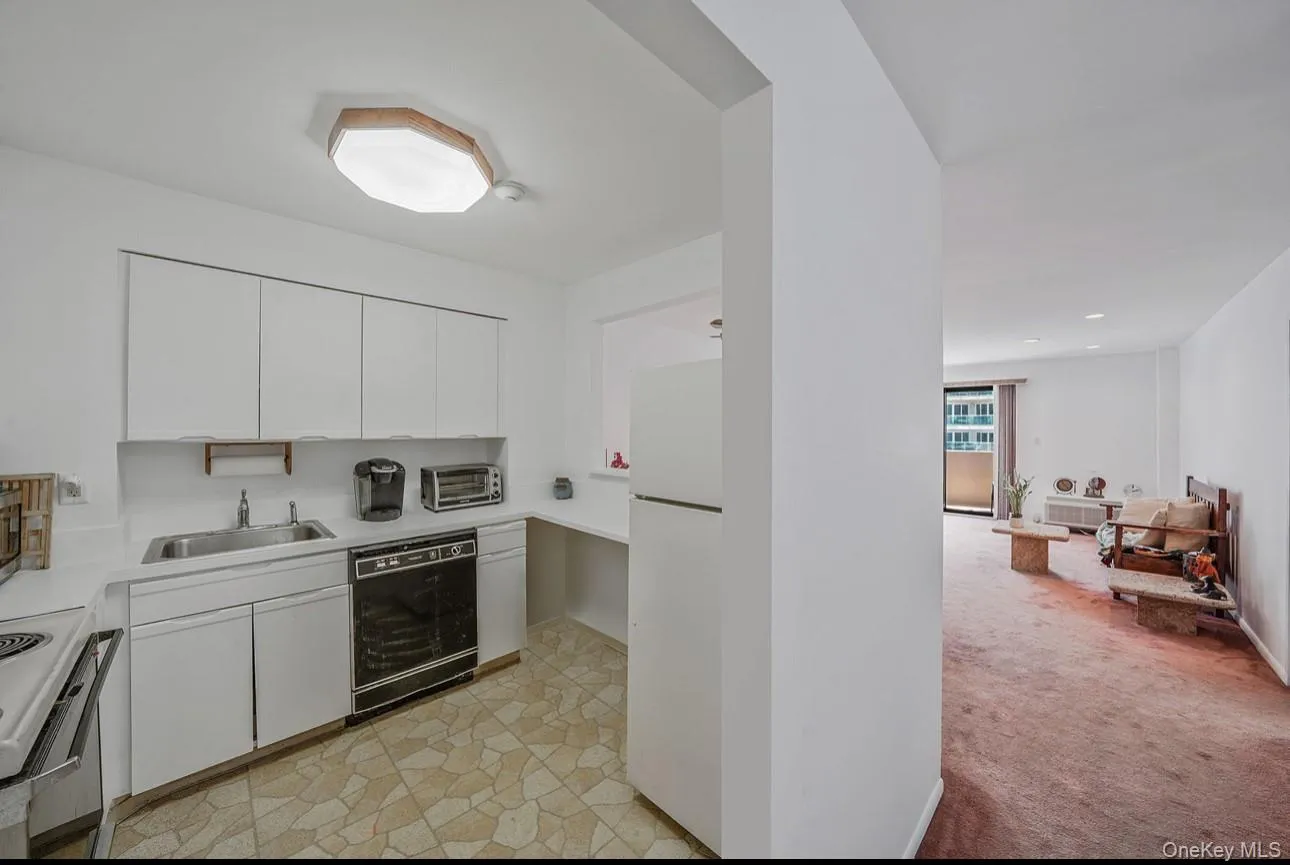 Kitchen featuring light countertops, light colored carpet, white cabinets, and white appliances Kitchen featuring light countertops, light colored carpet, white cabinets, and white appliances