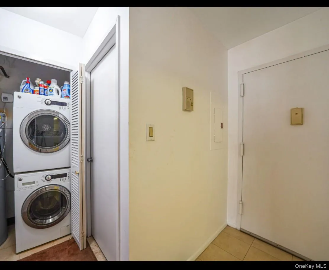 Laundry room with stacked washer / dryer, light tile patterned floors, and electric panel Laundry room with stacked washer / dryer, light tile patterned floors, and electric panel