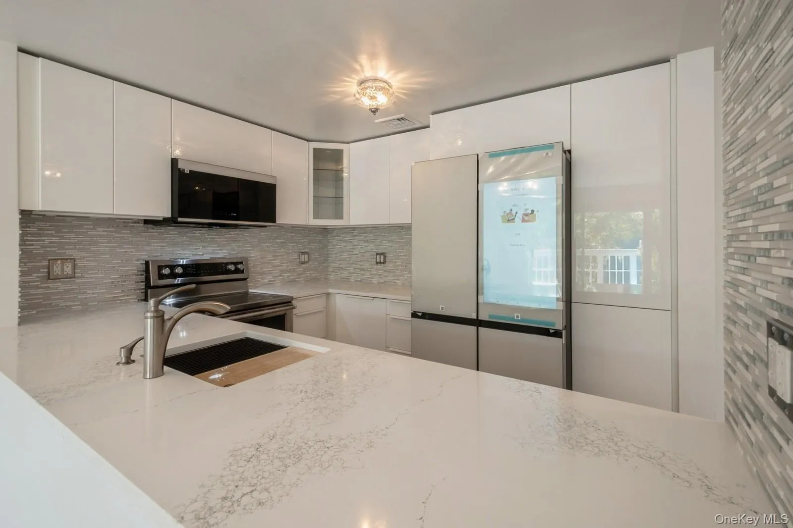 Kitchen with stainless steel electric stove, freestanding refrigerator, backsplash, light stone counters, and glass insert cabinets Kitchen with stainless steel electric stove, freestanding refrigerator, backsplash, light stone counters, and glass insert cabinets