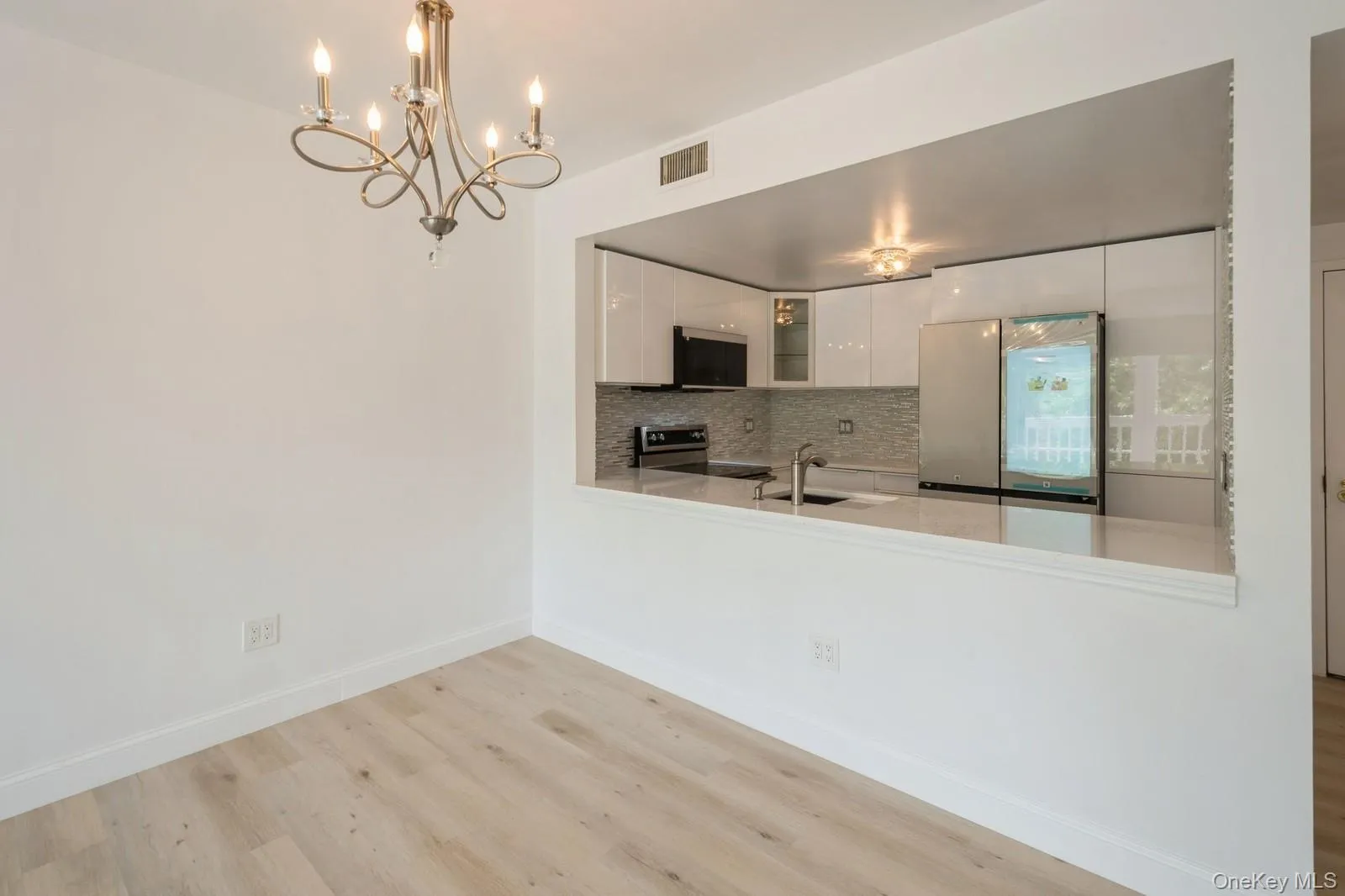 Kitchen featuring freestanding refrigerator, stainless steel electric stove, light wood-style floors, white cabinets, and a chandelier Kitchen featuring freestanding refrigerator, stainless steel electric stove, light wood-style floors, white cabinets, and a chandelier