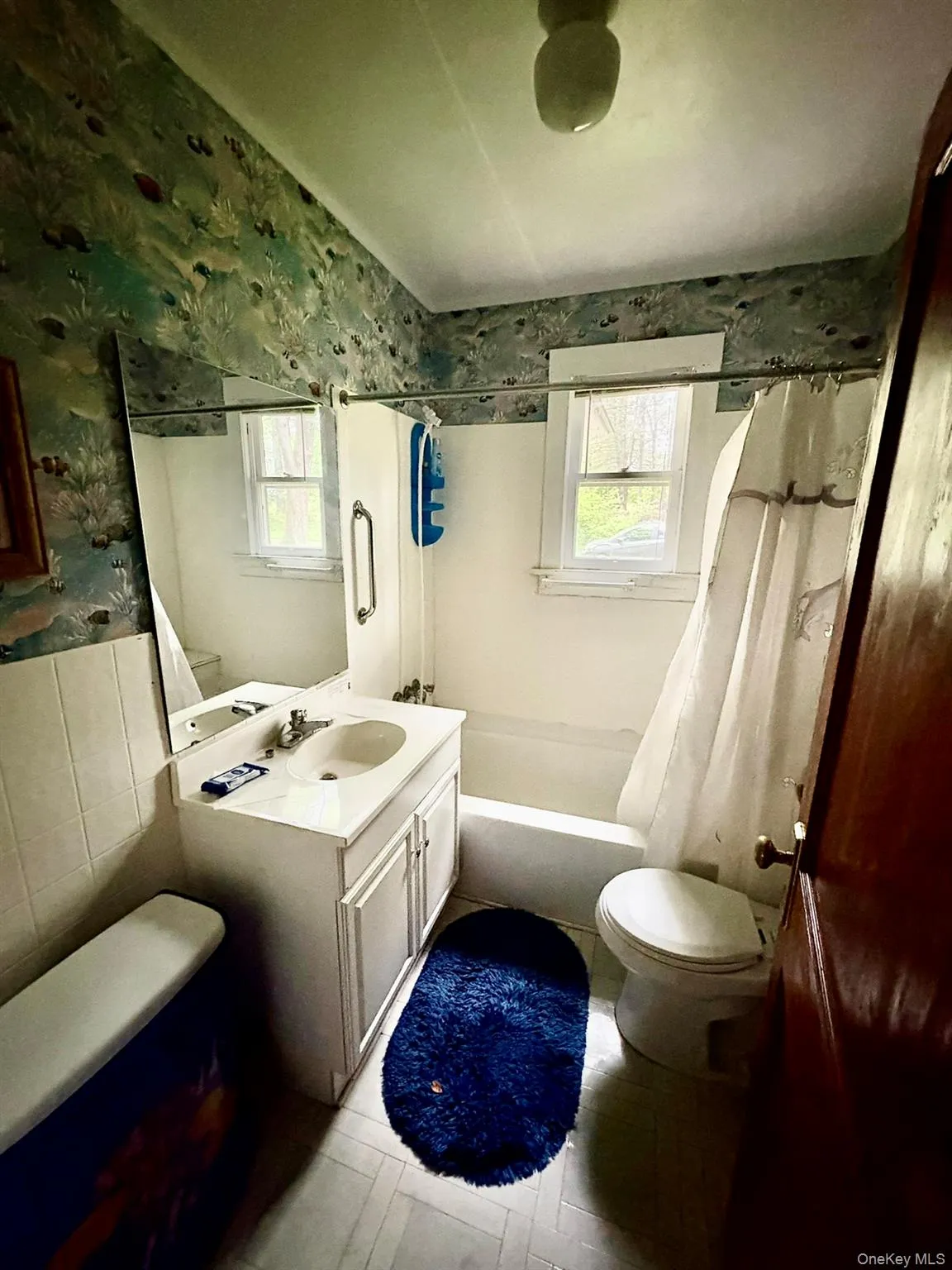 Bathroom with toilet, wallpapered walls, shower / tub combo, plenty of natural light, and vanity Bathroom with toilet, wallpapered walls, shower / tub combo, plenty of natural light, and vanity