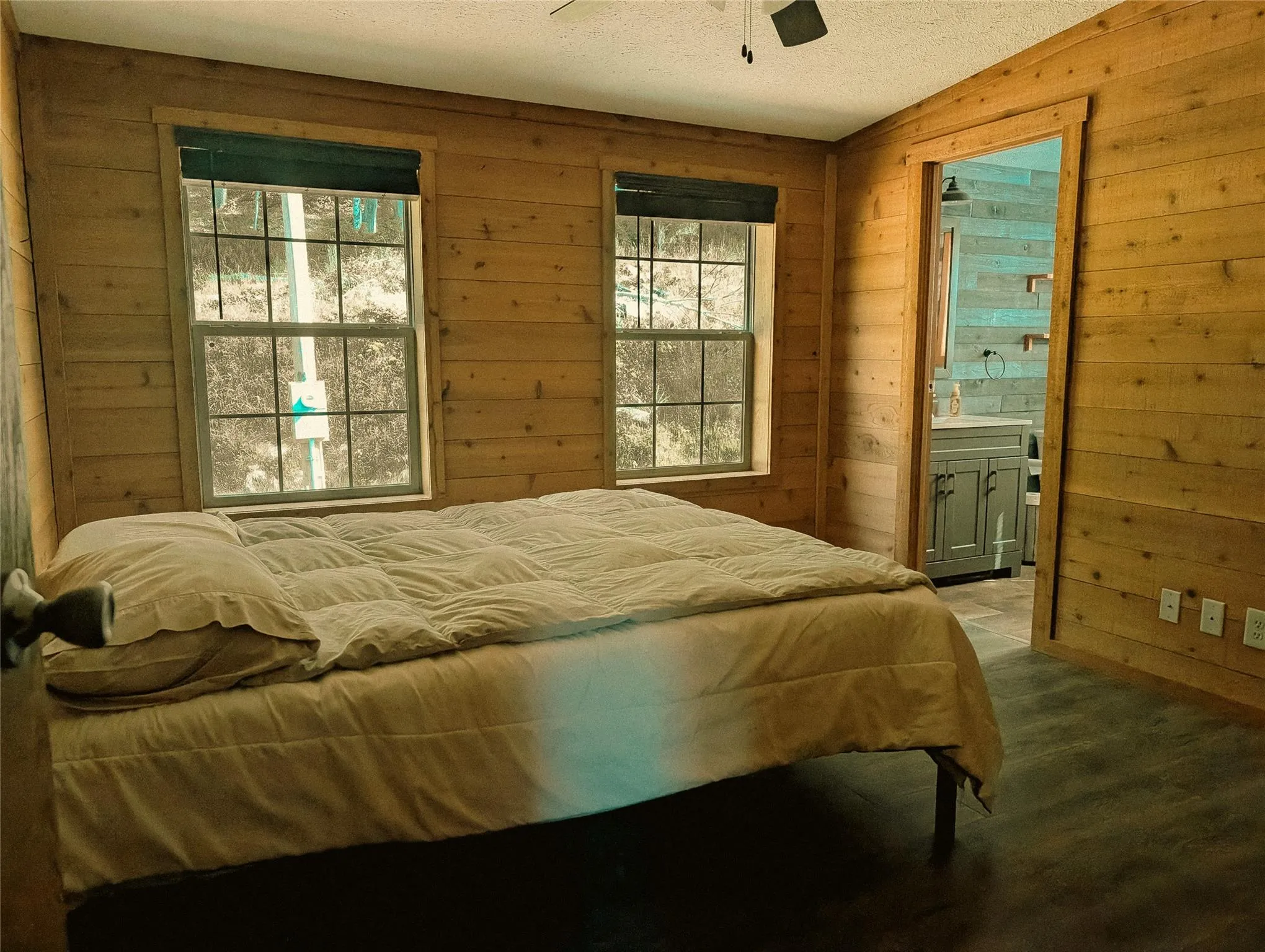 Bedroom featuring wood walls, ensuite bathroom, a textured ceiling, and a ceiling fan Bedroom featuring wood walls, ensuite bathroom, a textured ceiling, and a ceiling fan