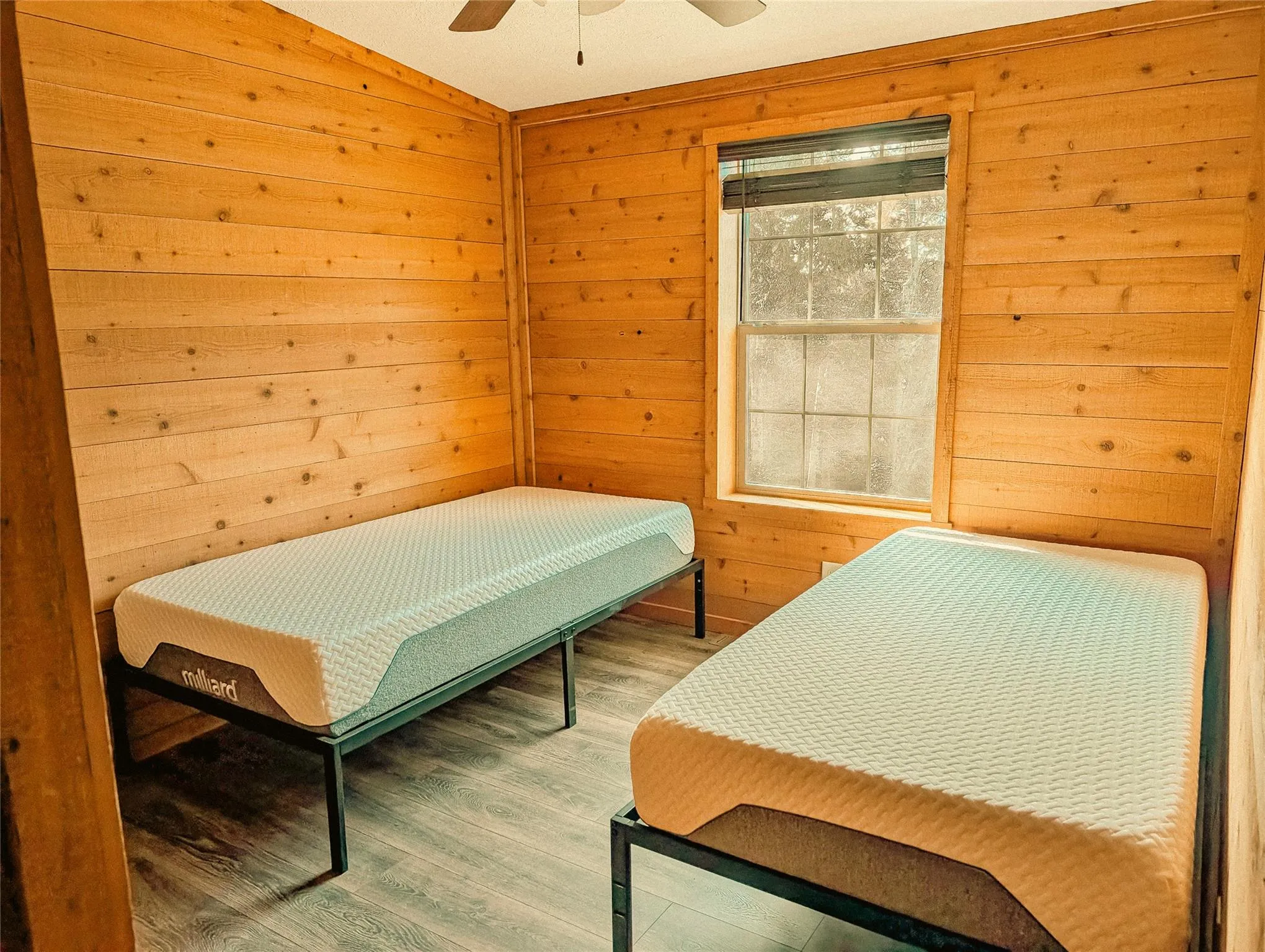 Bedroom with finished floors, wooden walls, two beds, and a ceiling fan Bedroom with finished floors, wooden walls, two beds, and a ceiling fan