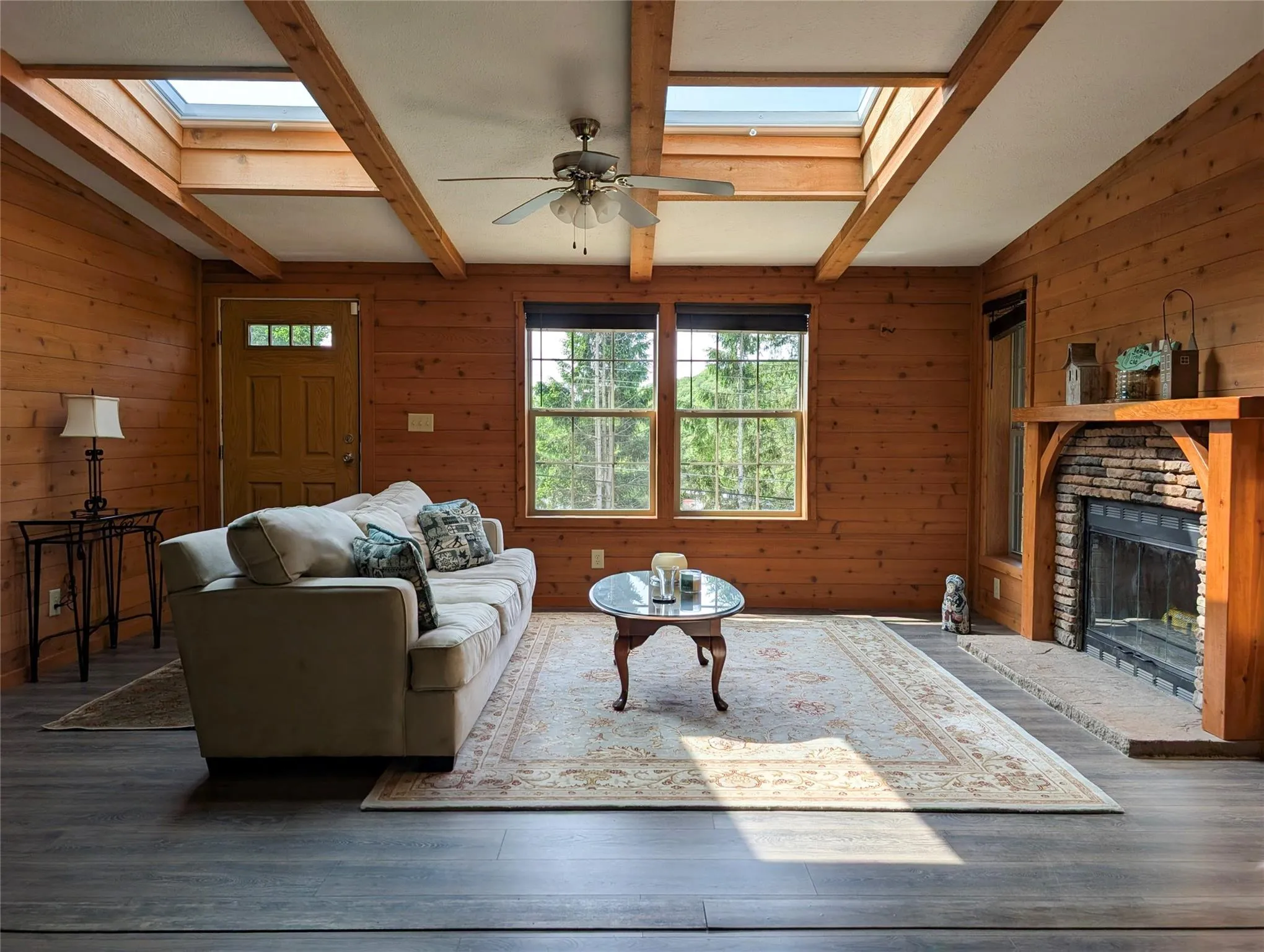 Living area featuring a skylight, wooden walls, beamed ceiling, wood finished floors, and ceiling fan Living area featuring a skylight, wooden walls, beamed ceiling, wood finished floors, and ceiling fan