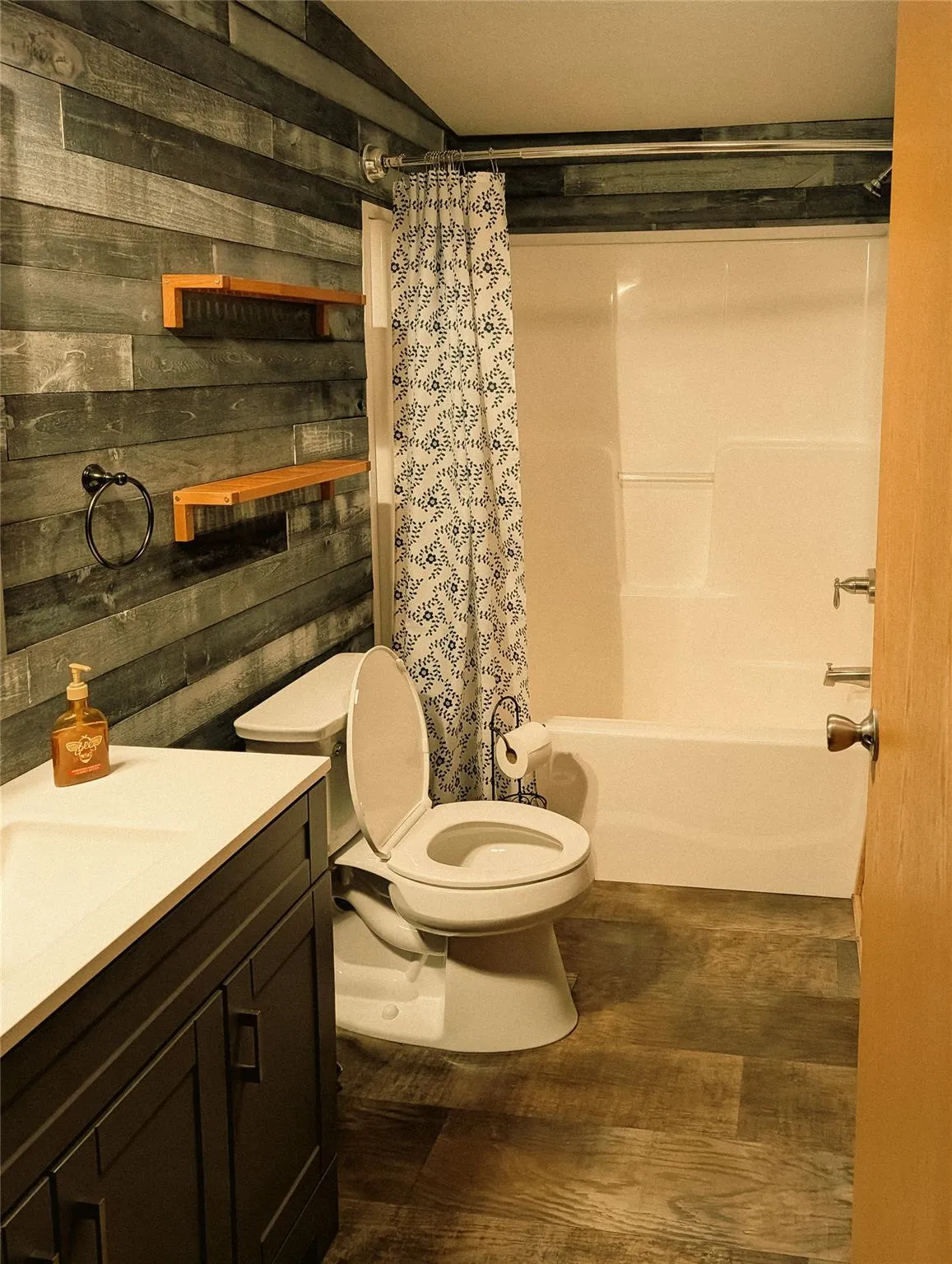 Bathroom with vanity, toilet, wood walls, shower / bath combo, and wood finished floors Bathroom with vanity, toilet, wood walls, shower / bath combo, and wood finished floors