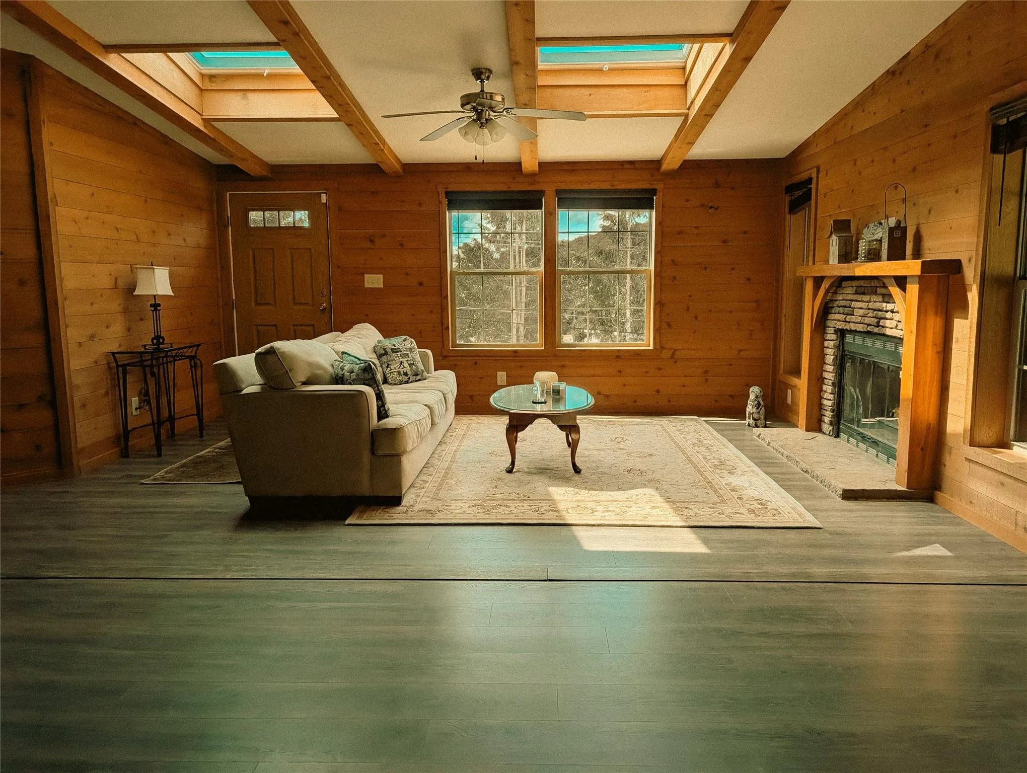 Living area with a skylight, wood walls, a fireplace, ceiling fan, and beam ceiling Living area with a skylight, wood walls, a fireplace, ceiling fan, and beam ceiling
