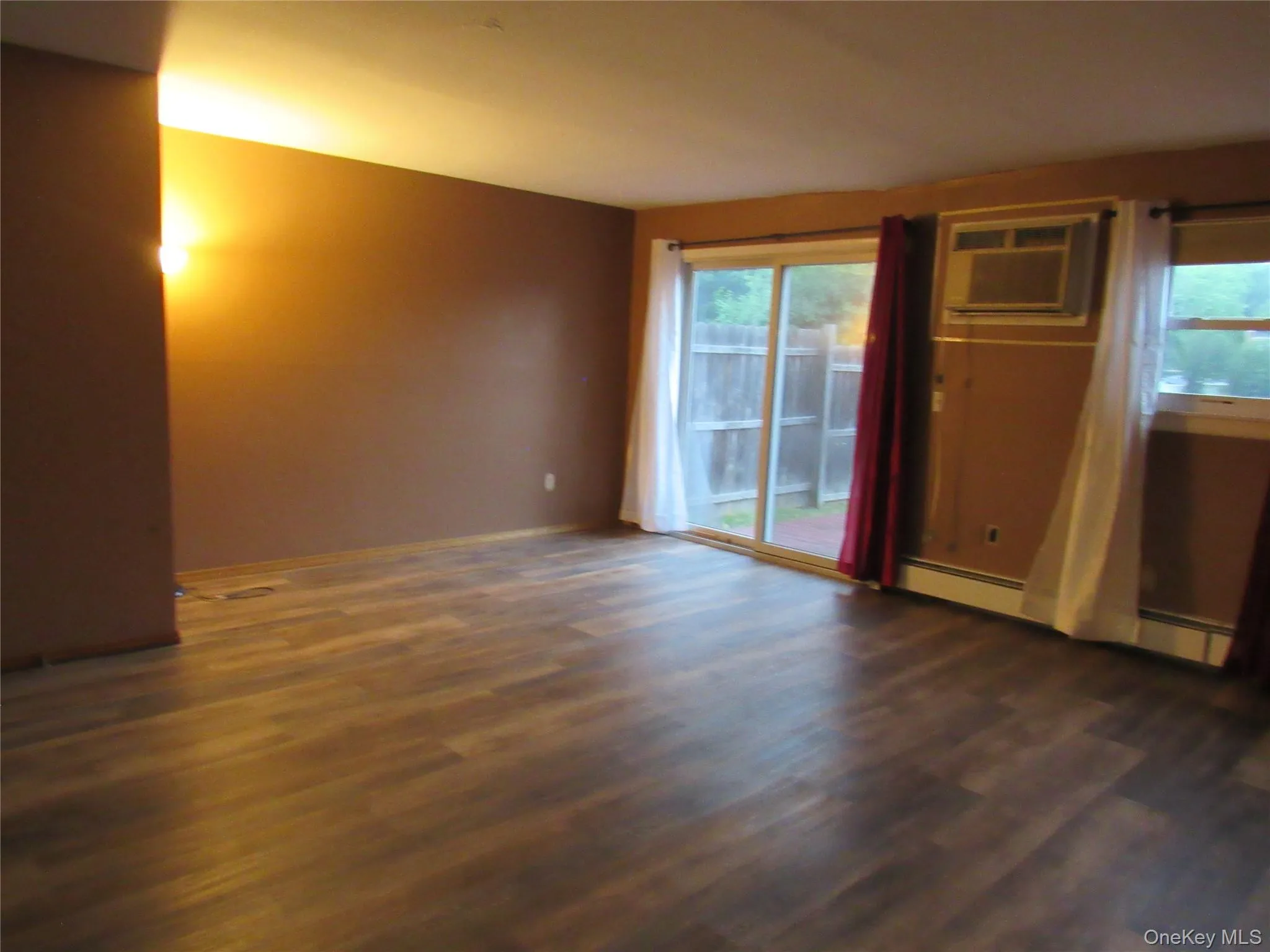 Unfurnished room featuring dark wood-style floors, an AC wall unit, and baseboard heating Unfurnished room featuring dark wood-style floors, an AC wall unit, and baseboard heating