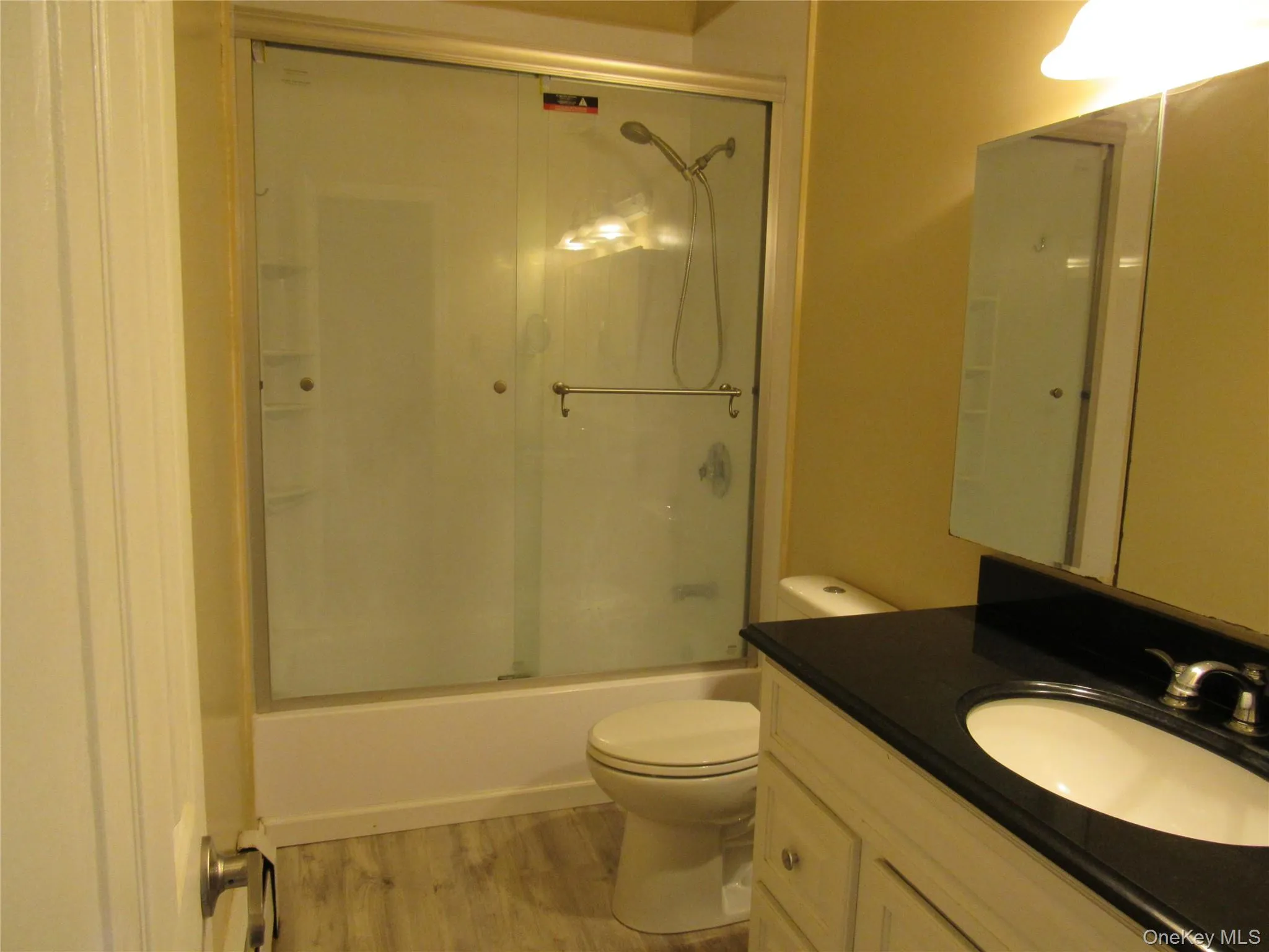 Full bathroom with vanity, wood finished floors, and bath / shower combo with glass door Full bathroom with vanity, wood finished floors, and bath / shower combo with glass door