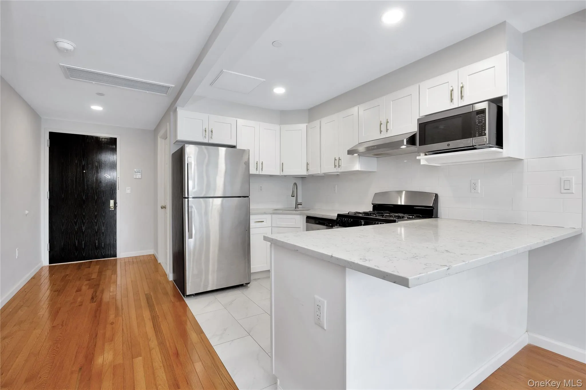 Kitchen featuring light stone countertops, white cabinetry, a peninsula, and stainless steel appliances Kitchen featuring light stone countertops, white cabinetry, a peninsula, and stainless steel appliances