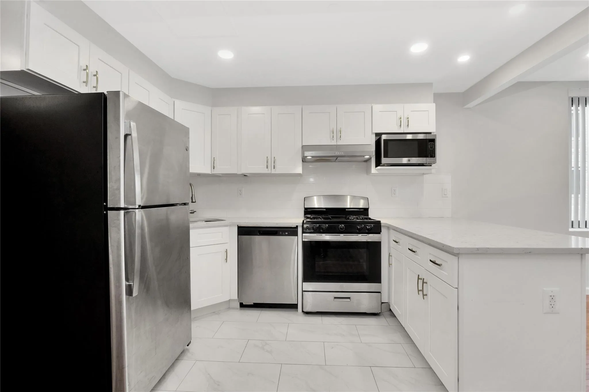 Kitchen with appliances with stainless steel finishes, a peninsula, under cabinet range hood, white cabinetry, and marble finish floor Kitchen with appliances with stainless steel finishes, a peninsula, under cabinet range hood, white cabinetry, and marble finish floor