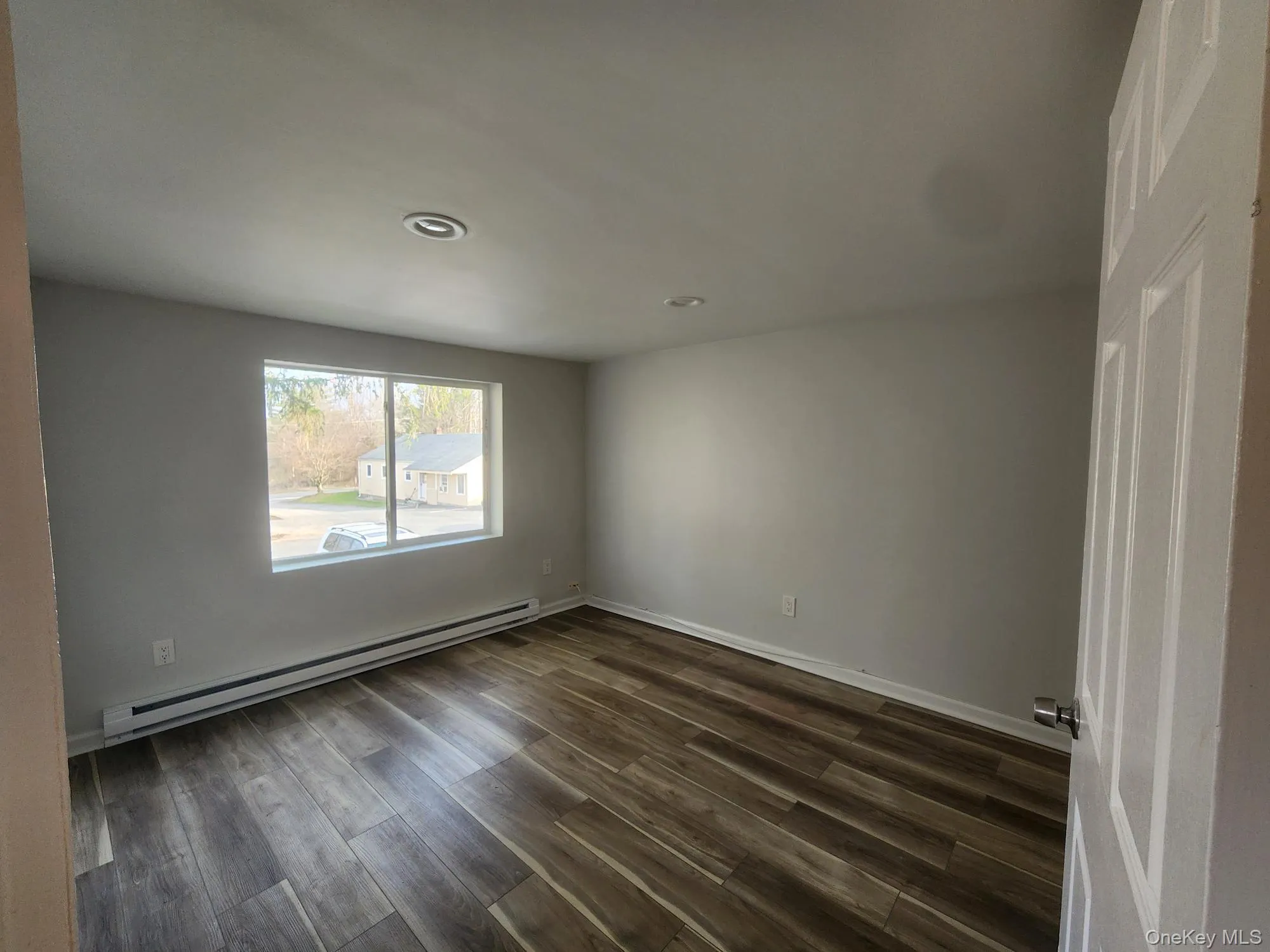 Empty room with a baseboard heating unit, dark wood-type flooring, recessed lighting, and baseboards Empty room with a baseboard heating unit, dark wood-type flooring, recessed lighting, and baseboards