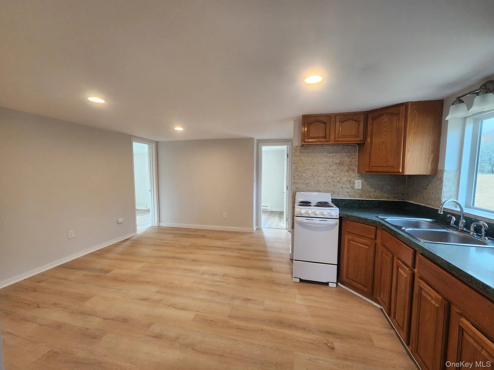 Kitchen with white range with electric cooktop, a sink, dark countertops, backsplash, and brown cabinetry Kitchen with white range with electric cooktop, a sink, dark countertops, backsplash, and brown cabinetry