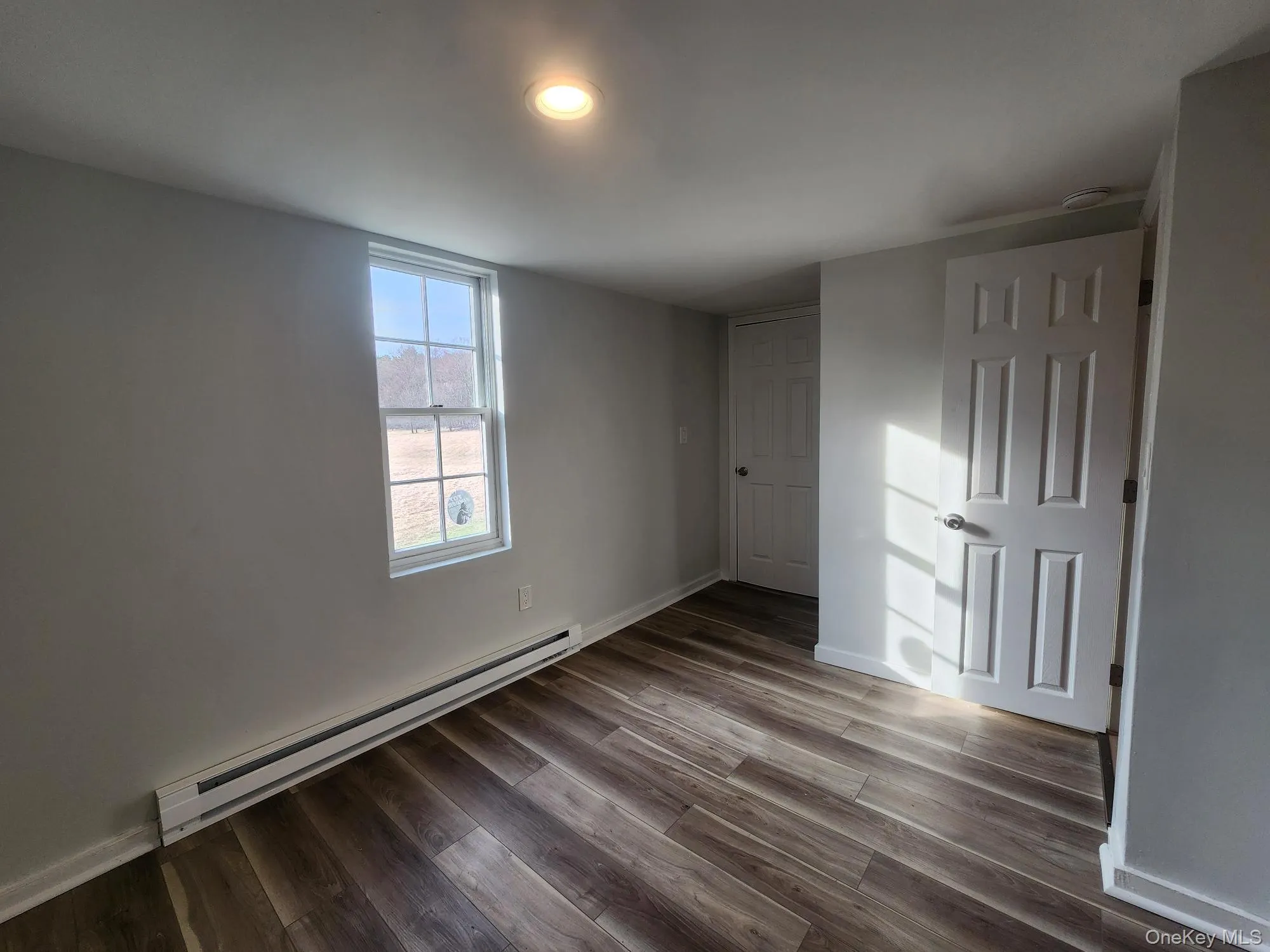 Unfurnished bedroom with a baseboard radiator, dark wood finished floors, and baseboards Unfurnished bedroom with a baseboard radiator, dark wood finished floors, and baseboards