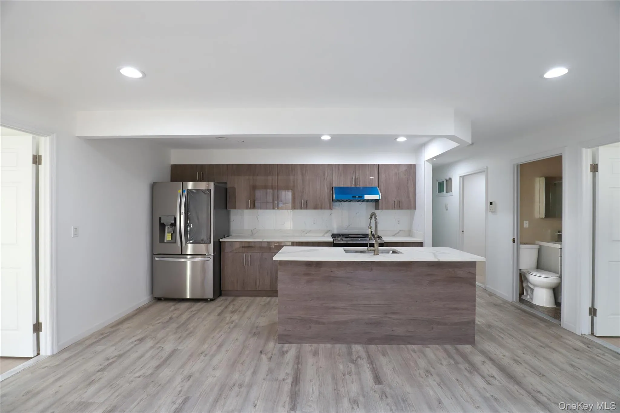 Kitchen with stainless steel fridge with ice dispenser, an island with sink, light wood-type flooring, tasteful backsplash, and recessed lighting Kitchen with stainless steel fridge with ice dispenser, an island with sink, light wood-type flooring, tasteful backsplash, and recessed lighting