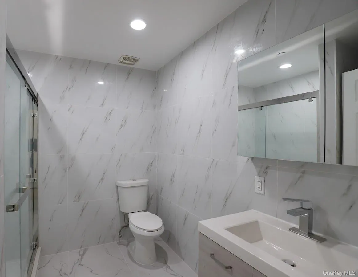 Full bath featuring a marble finish shower, tile walls, vanity, and marble tiled floors Full bath featuring a marble finish shower, tile walls, vanity, and marble tiled floors