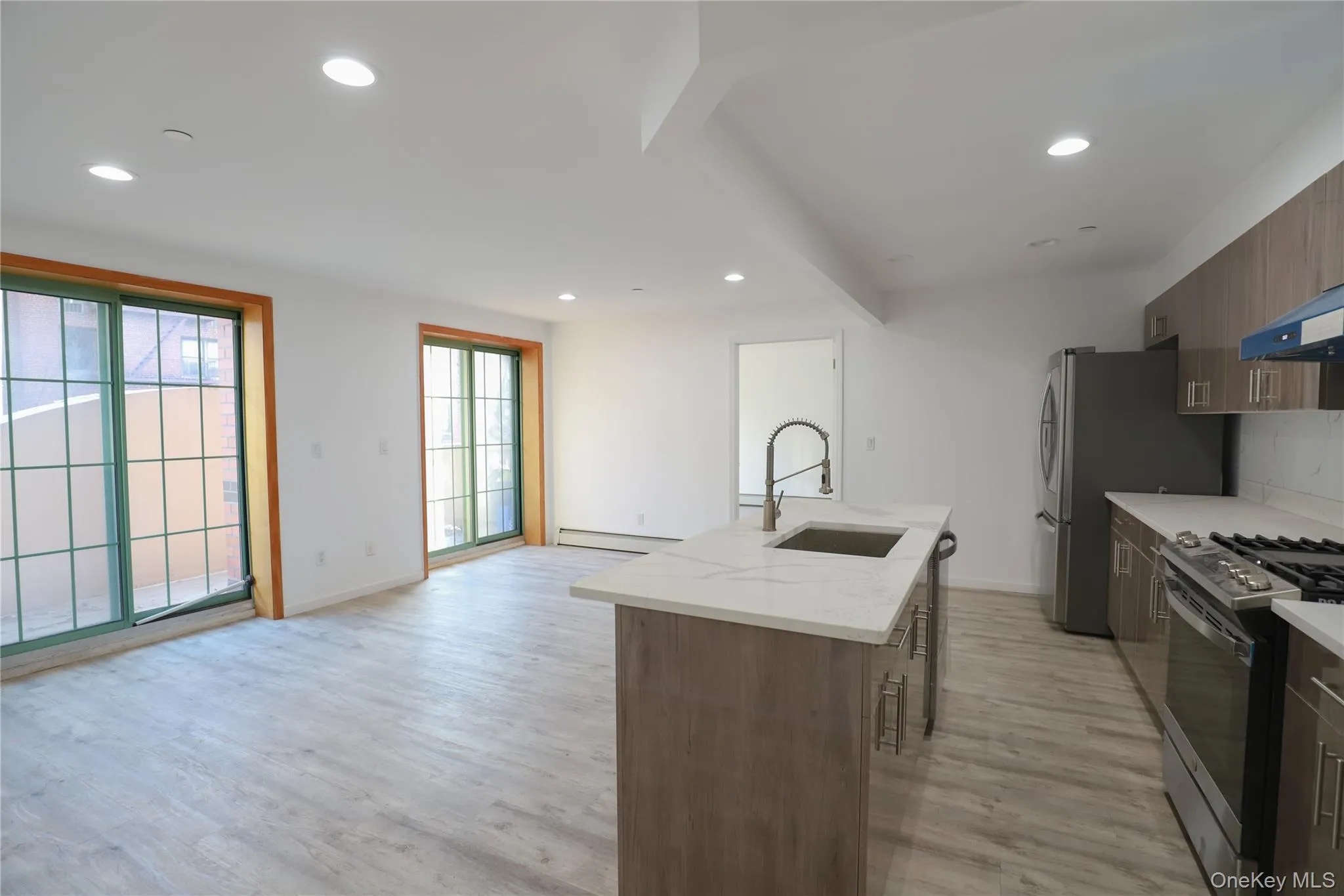 Kitchen featuring recessed lighting, light wood-type flooring, light stone countertops, an island with sink, and appliances with stainless steel finishes Kitchen featuring recessed lighting, light wood-type flooring, light stone countertops, an island with sink, and appliances with stainless steel finishes