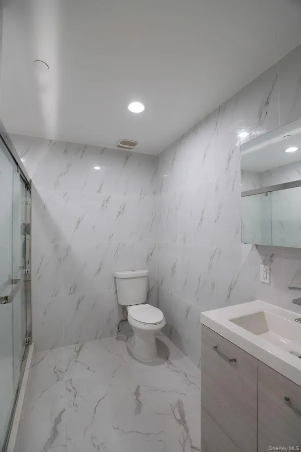 Bathroom with a marble finish shower, tile walls, marble tiled floors, vanity, and recessed lighting Bathroom with a marble finish shower, tile walls, marble tiled floors, vanity, and recessed lighting