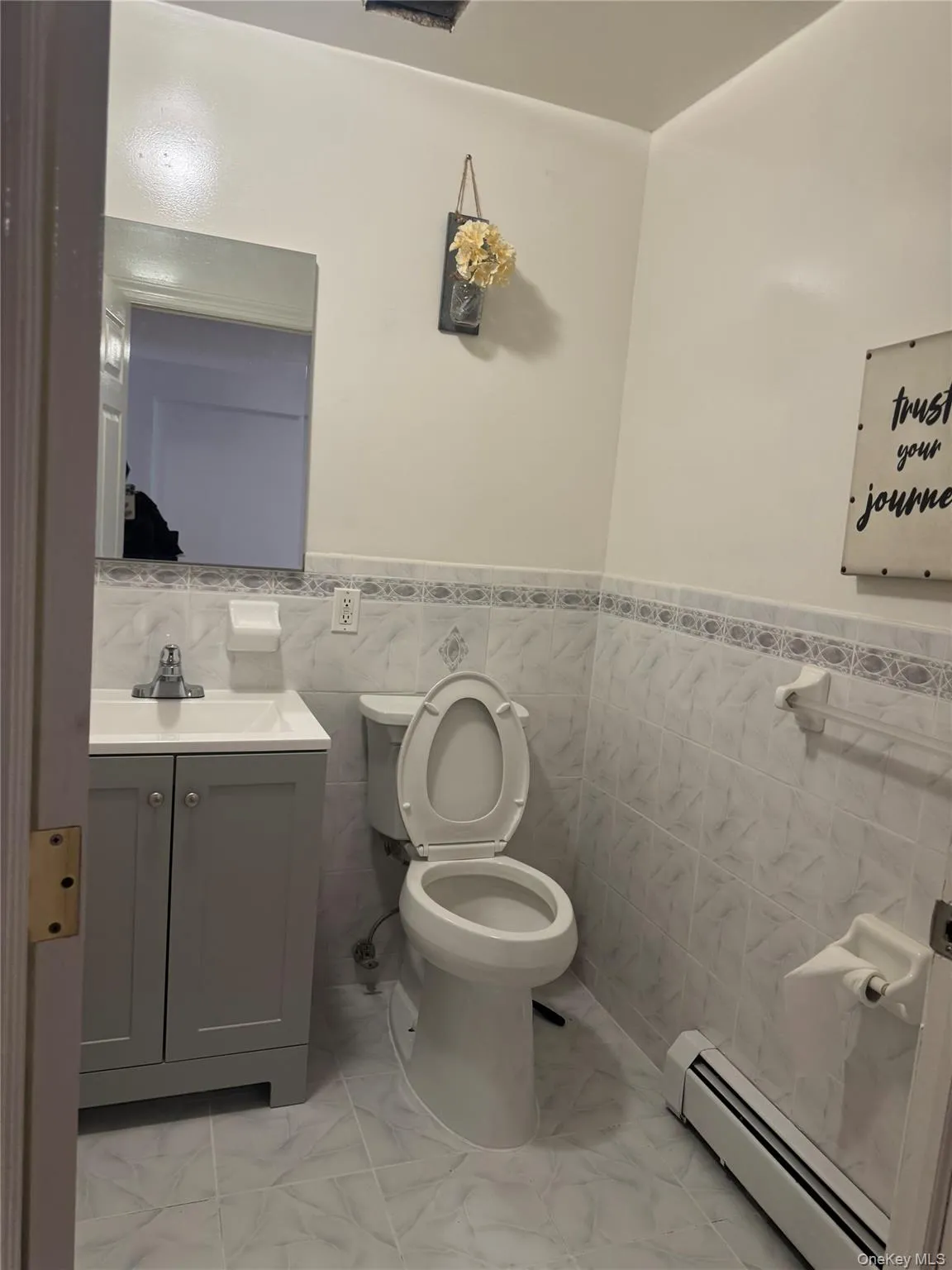 Bathroom with baseboard heating, vanity, wainscoting, toilet, and tile walls Bathroom with baseboard heating, vanity, wainscoting, toilet, and tile walls