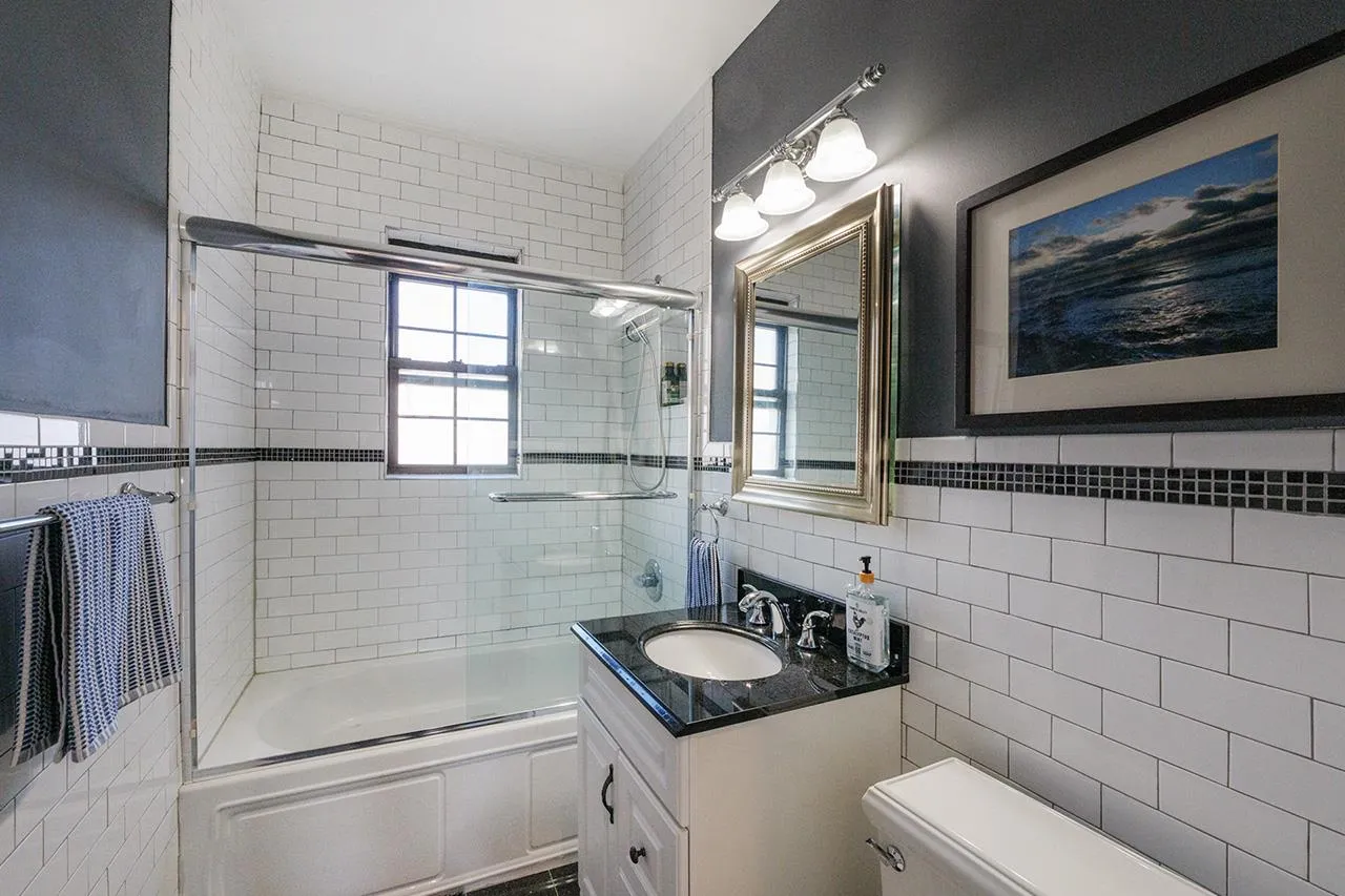 Bathroom with tile walls, bath / shower combo with glass door, vanity, and toilet Bathroom with tile walls, bath / shower combo with glass door, vanity, and toilet