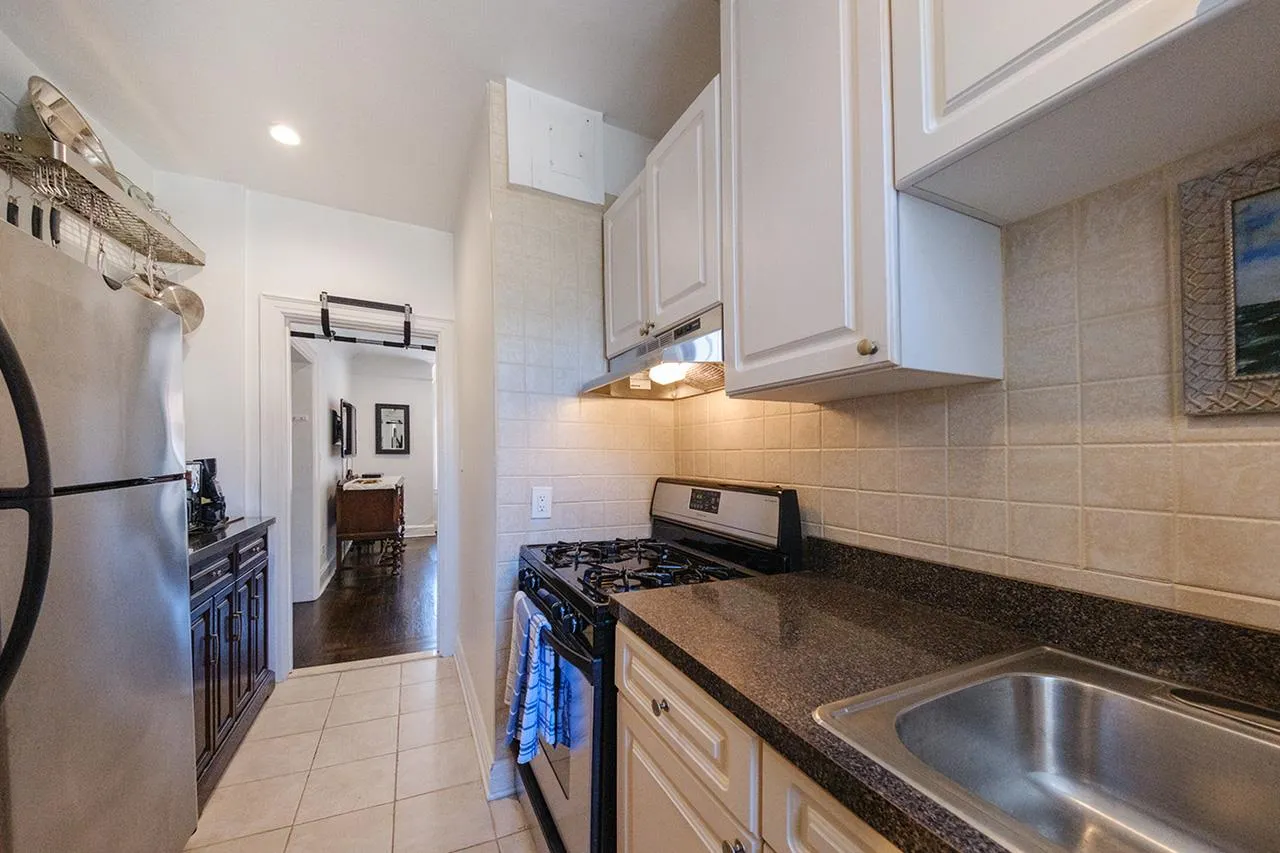 Kitchen featuring stainless steel appliances, under cabinet range hood, light tile patterned floors, backsplash, and a barn door Kitchen featuring stainless steel appliances, under cabinet range hood, light tile patterned floors, backsplash, and a barn door