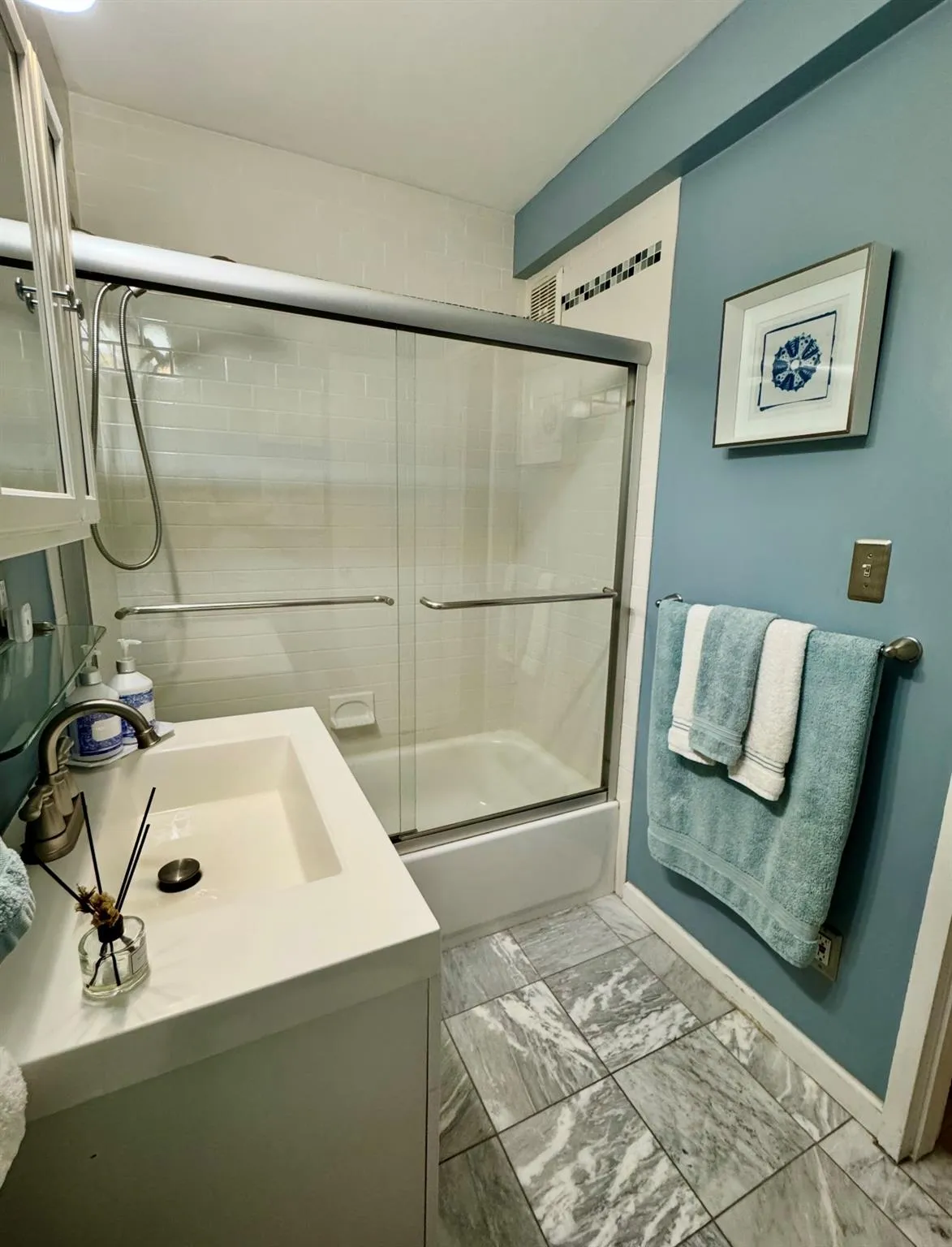 Bathroom featuring vanity, shower / bath combination with glass door, marble look tile flooring, and baseboards Bathroom featuring vanity, shower / bath combination with glass door, marble look tile flooring, and baseboards