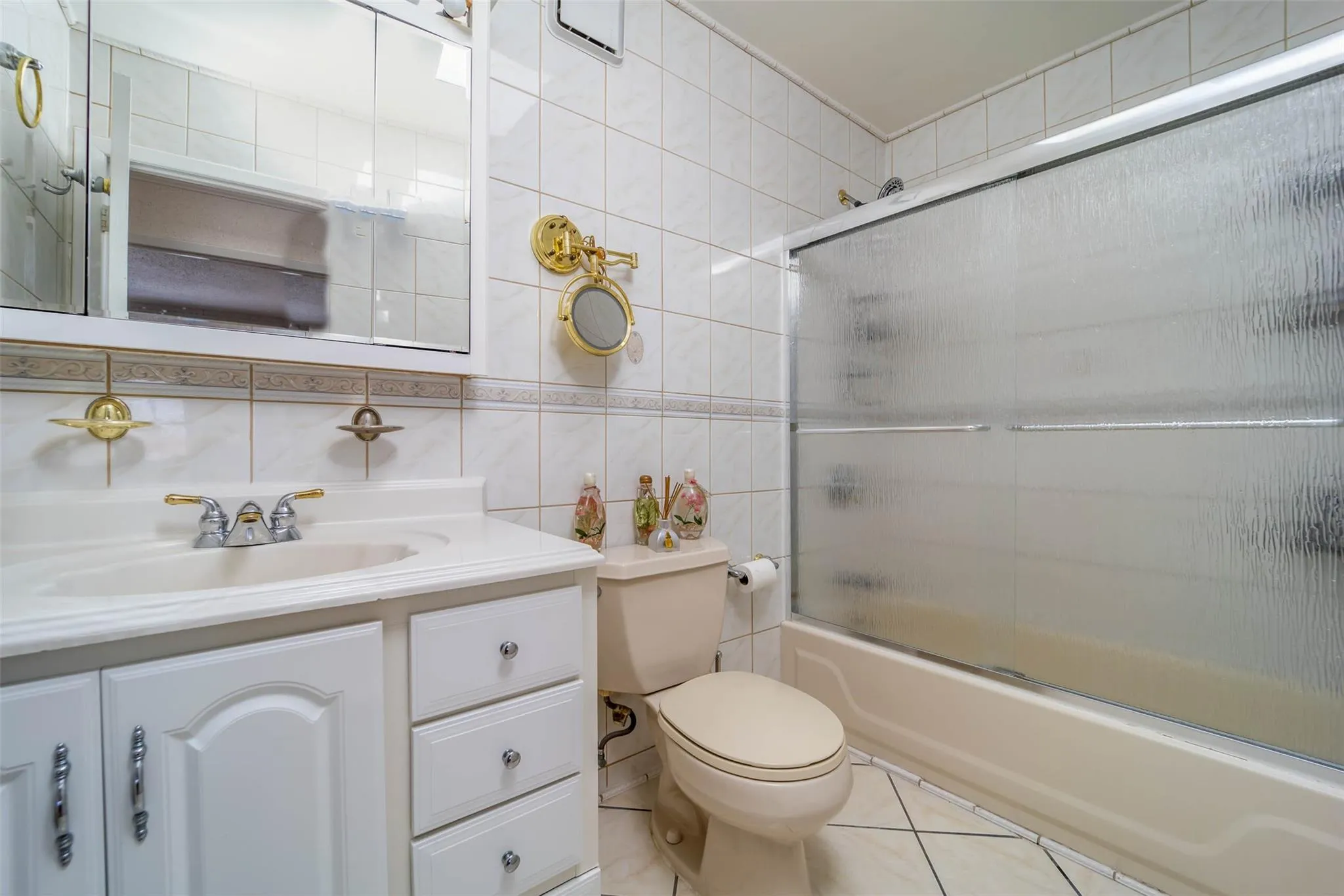 Full bath with tile walls, vanity, bath / shower combo with glass door, toilet, and tile patterned floors Full bath with tile walls, vanity, bath / shower combo with glass door, toilet, and tile patterned floors