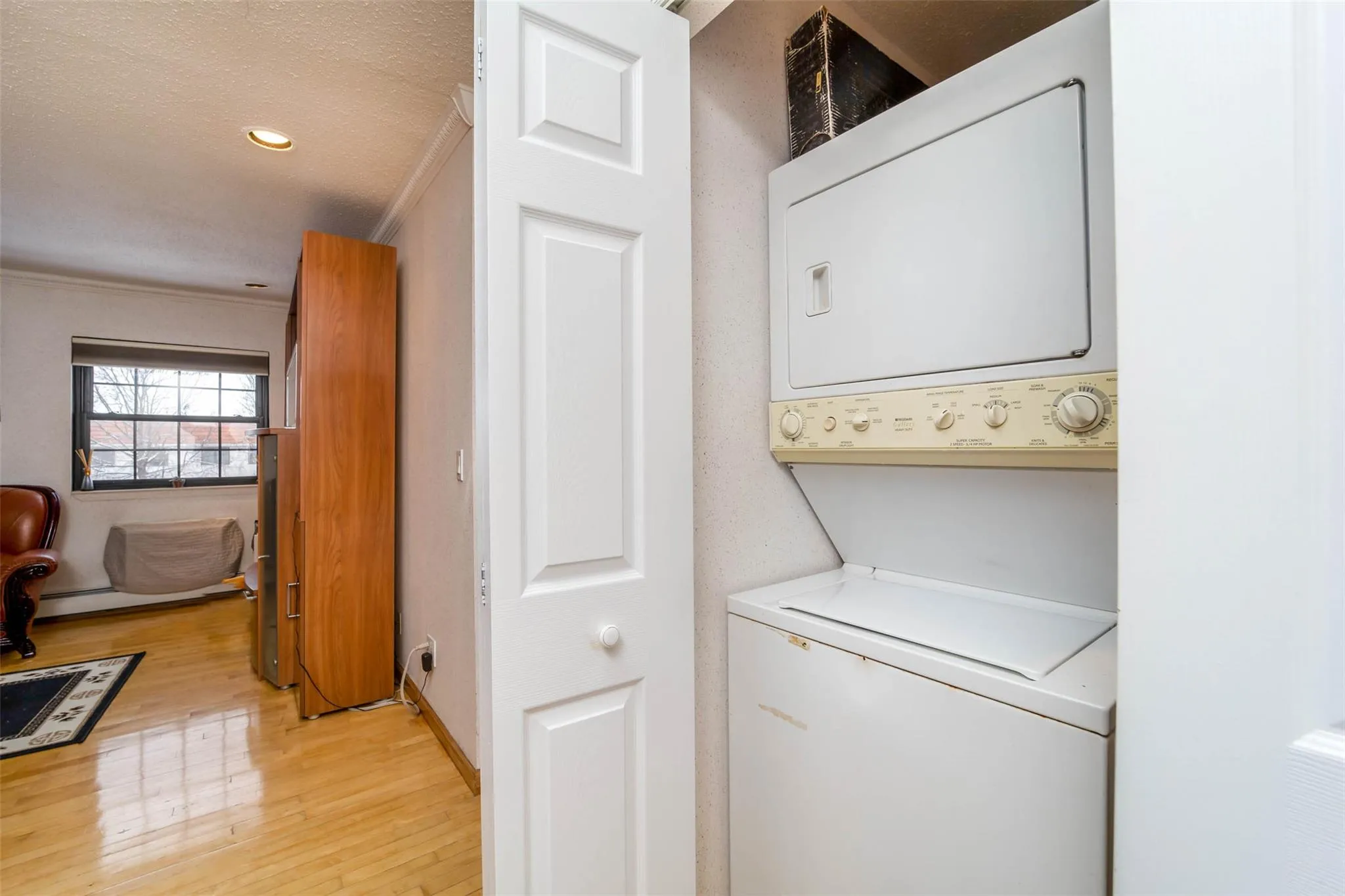 Washroom with stacked washer and clothes dryer, light wood-type flooring, ornamental molding, recessed lighting, and a textured ceiling Washroom with stacked washer and clothes dryer, light wood-type flooring, ornamental molding, recessed lighting, and a textured ceiling