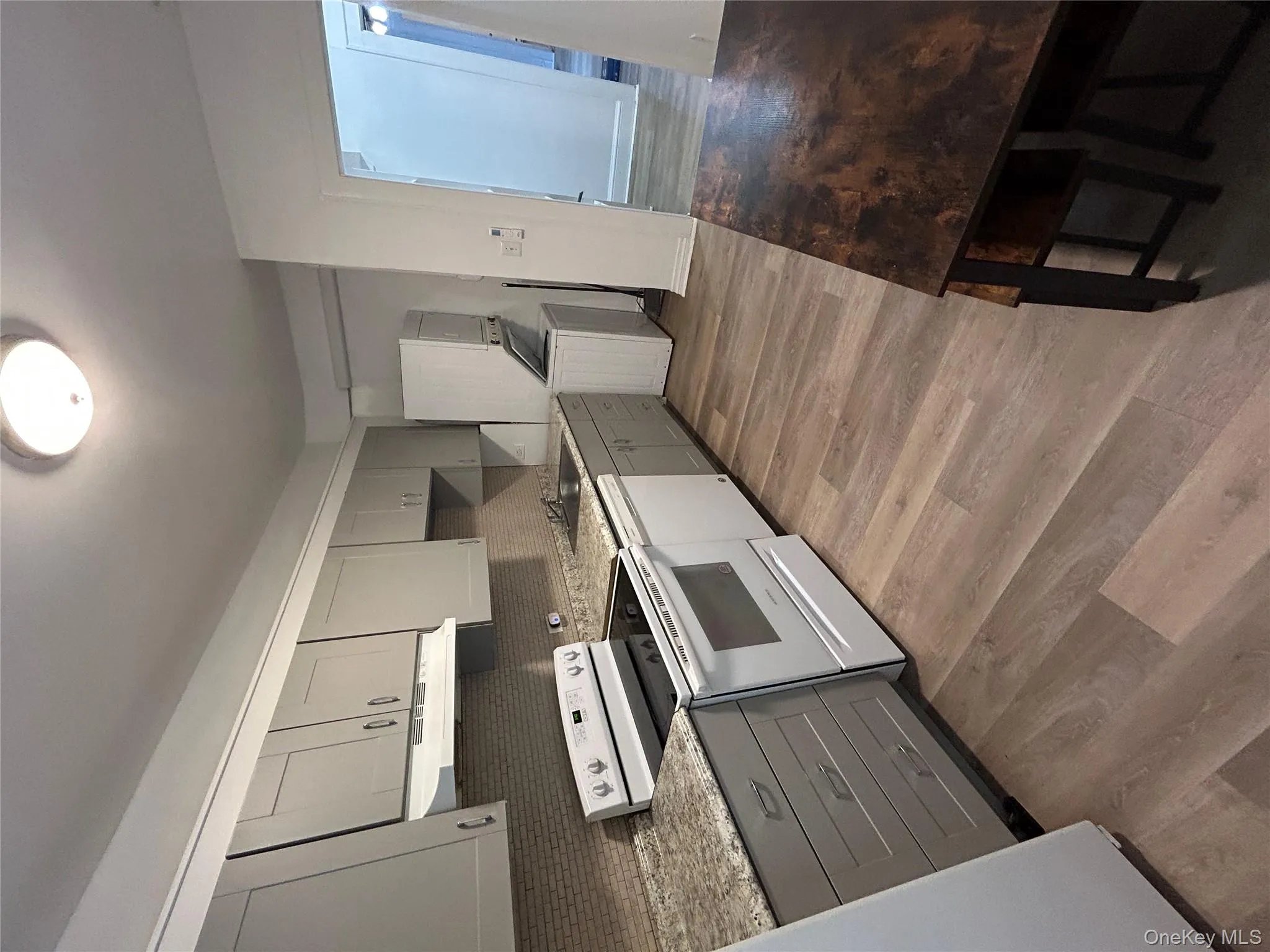 Kitchen with gray cabinetry, stove, backsplash, and stacked washer / drying machine Kitchen with gray cabinetry, stove, backsplash, and stacked washer / drying machine