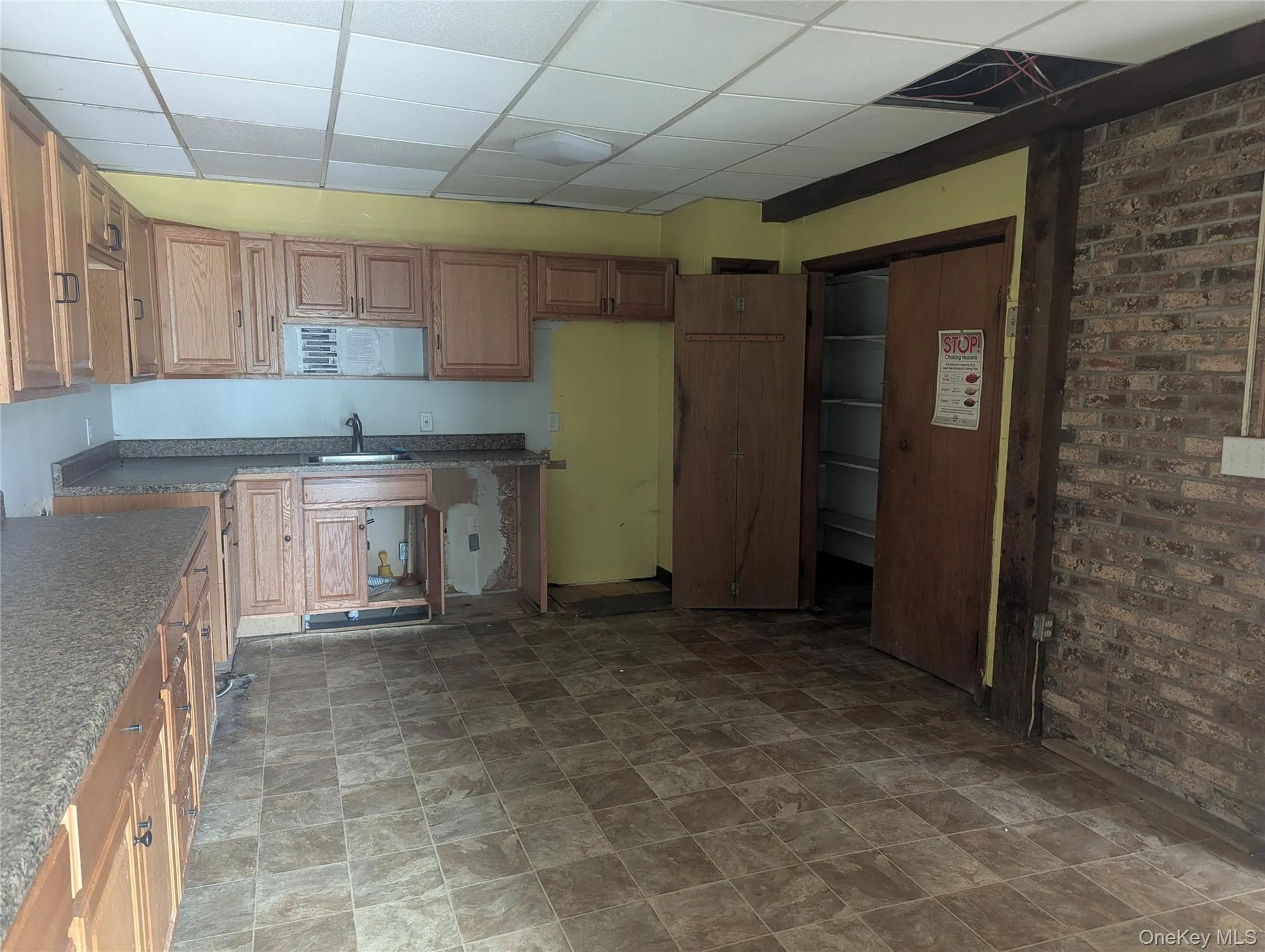 Kitchen with a paneled ceiling, brick wall, and stone finish floors Kitchen with a paneled ceiling, brick wall, and stone finish floors