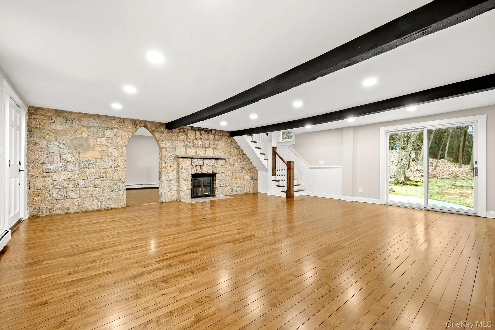 Living room featuring beamed ceiling, stairway,  wood floors, recessed lighting, and arched doorway, sliders out to patio and yard Living room featuring beamed ceiling, stairway,  wood floors, recessed lighting, and arched doorway, sliders out to patio and yard
